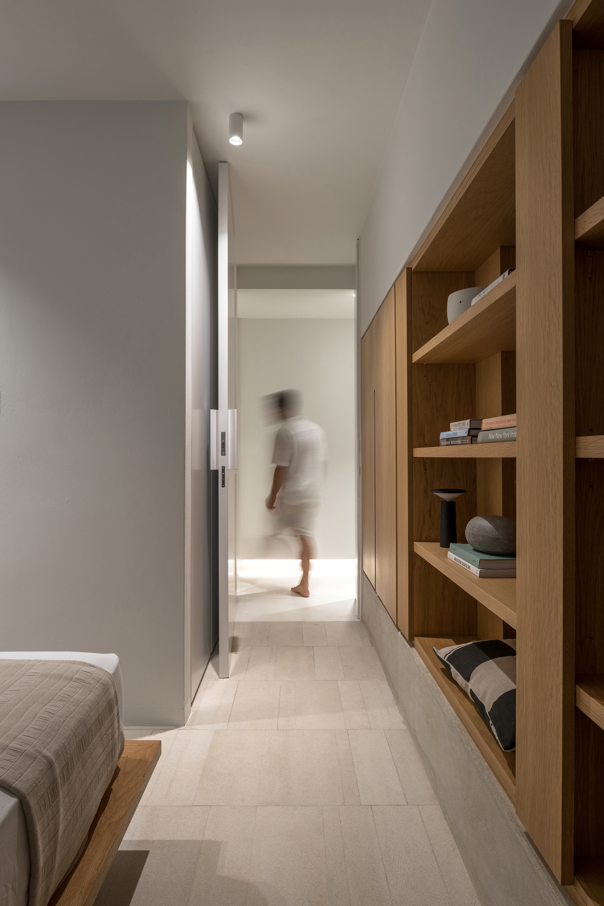 Narrow hallway with oak shelving along one wall and a blurred figure moving through distant doorway