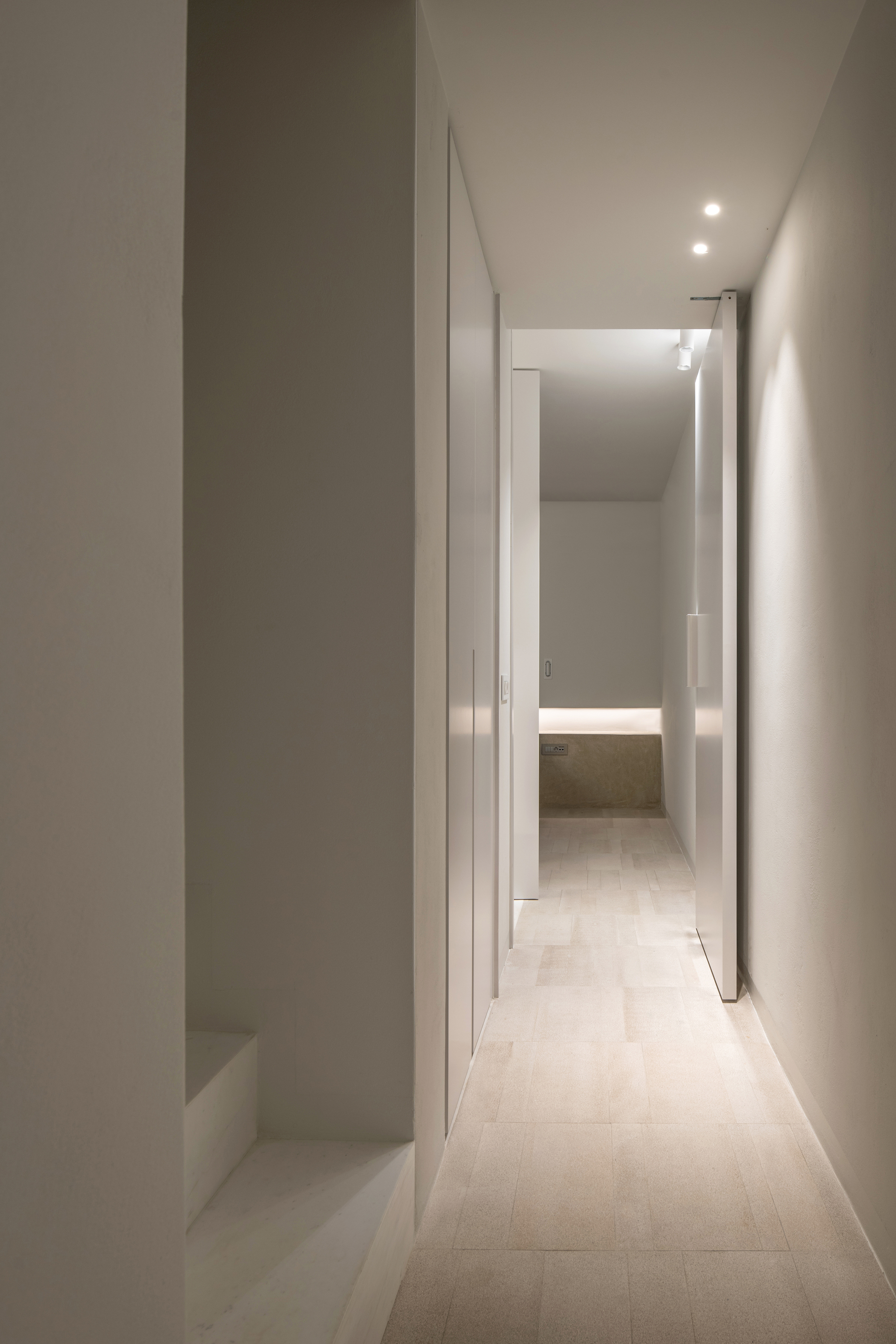 Long corridor view through layered white doorways with concealed lighting strips at floor level