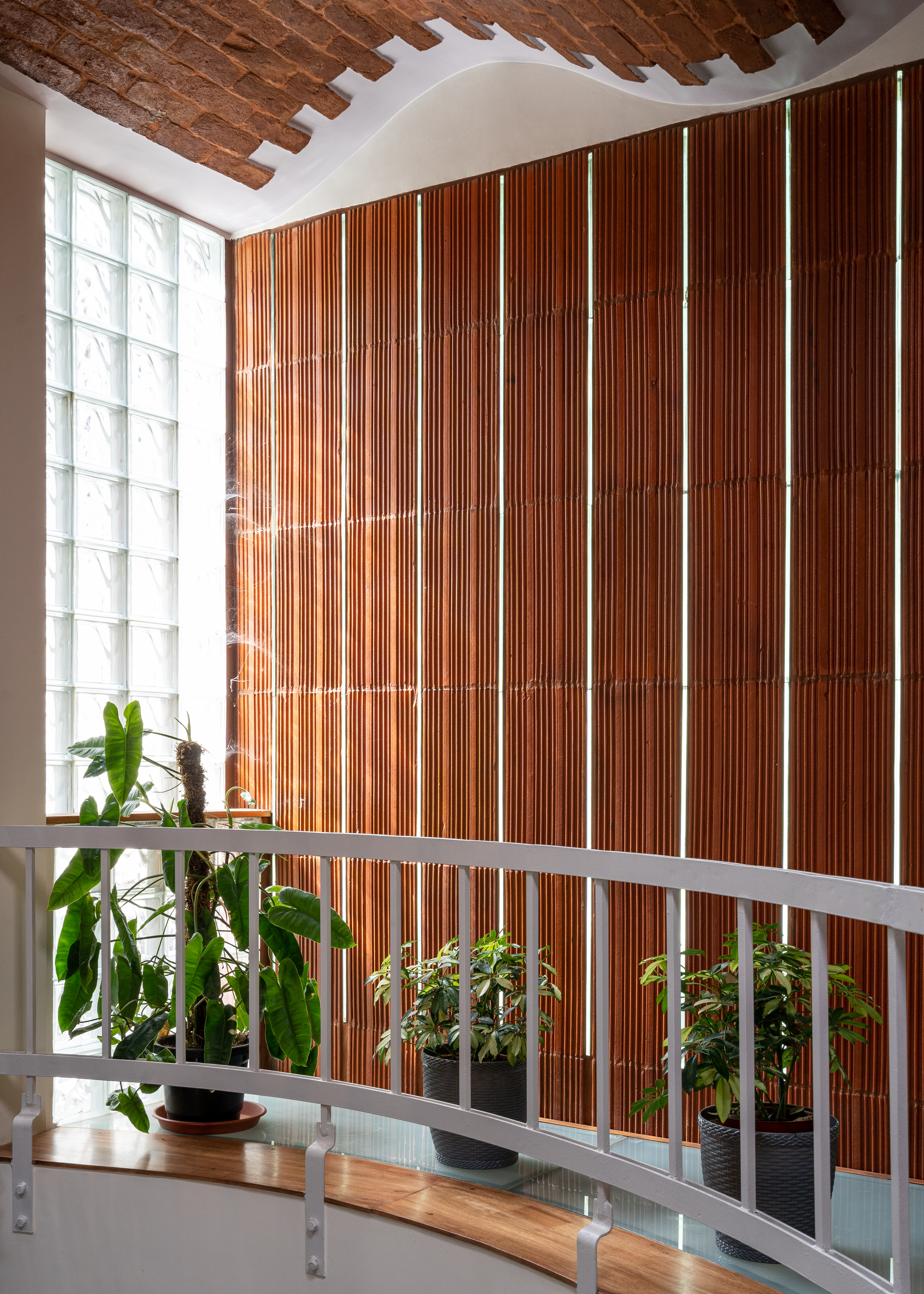 Vertical wood slat wall behind a white railing with potted plants and glass block window