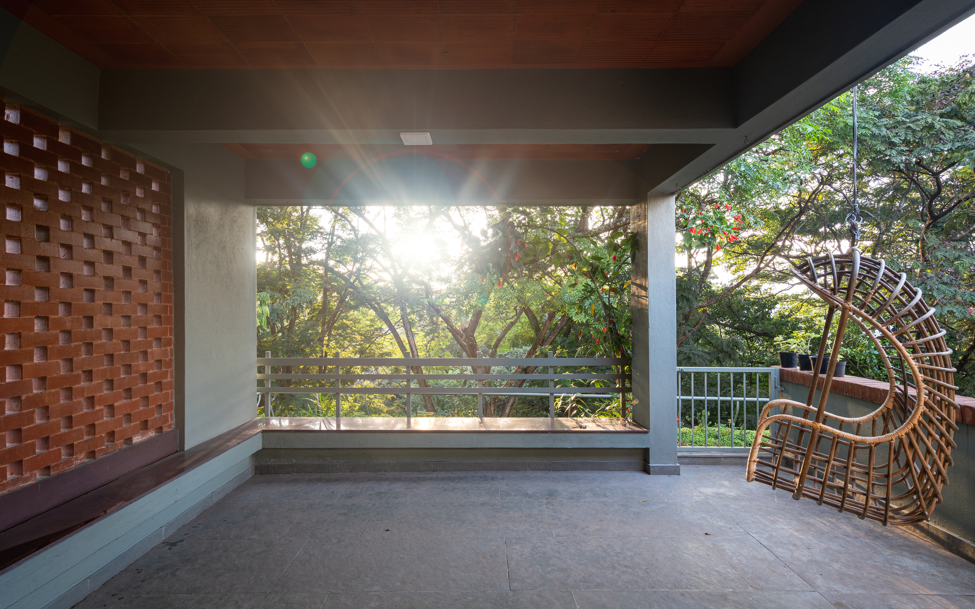 Open terrace with chequered brick screen wall, concrete soffit and wicker chair facing treetops