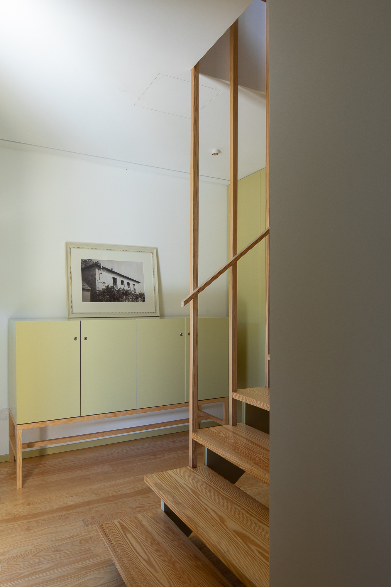 Open timber staircase ascending beside pale green built-in cabinetry and a framed photograph