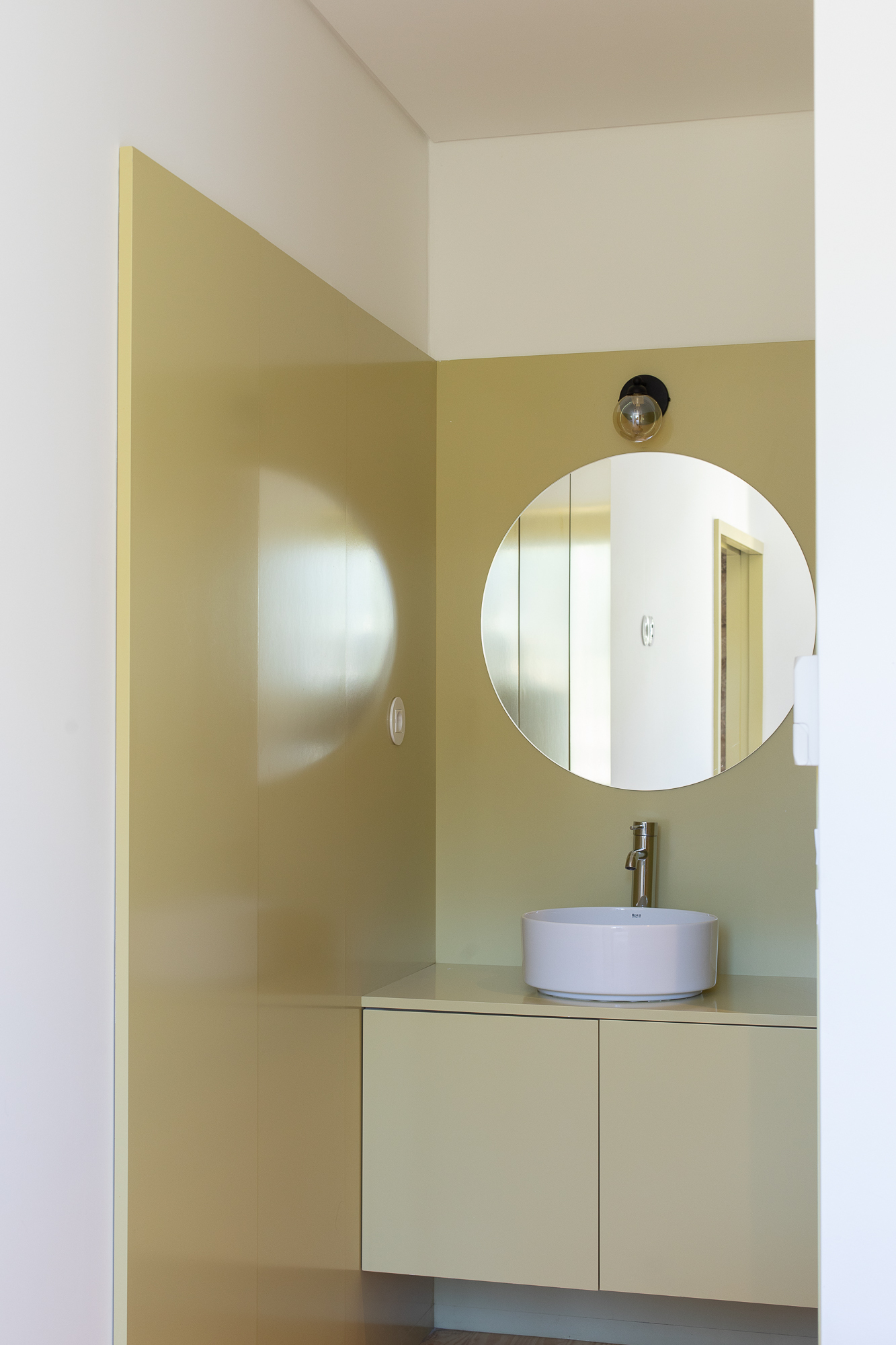 Bathroom vanity with circular mirror and vessel sink set against pale green tile