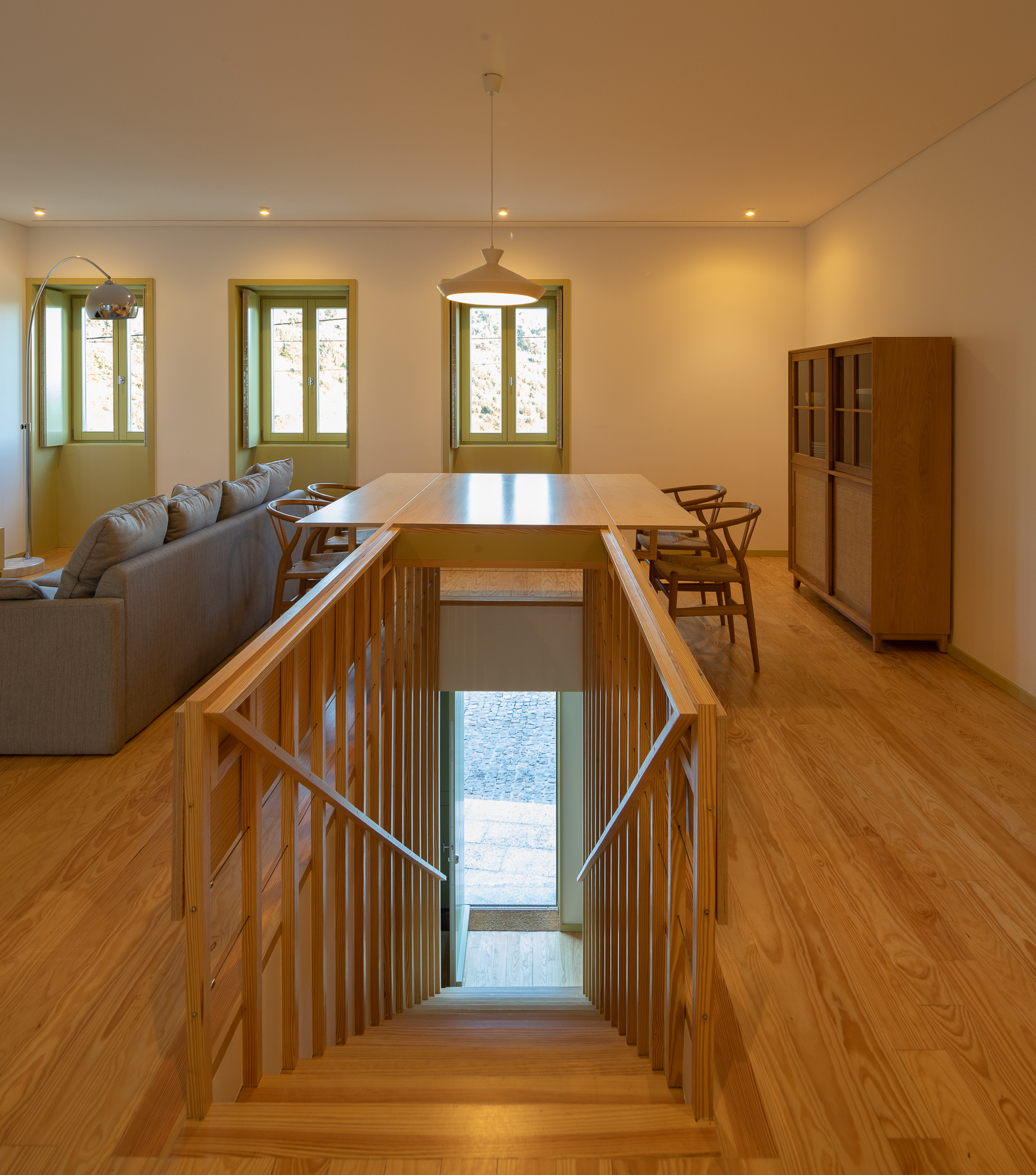 Timber staircase descending through an opening in the floor with vertical slatted balustrade and view to door below