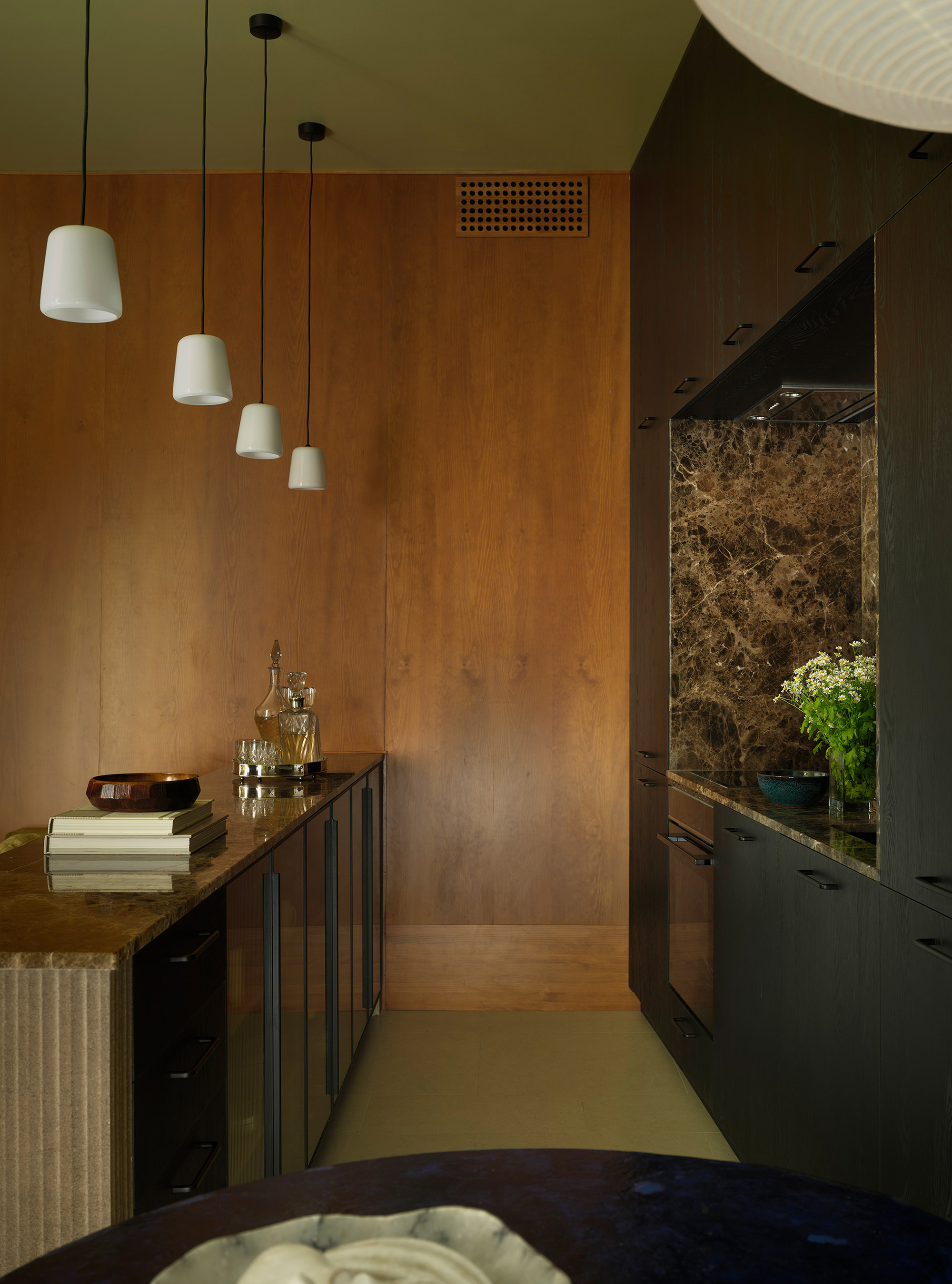 Kitchen with copper-clad wall panels, white pendant lights, and dark cabinetry beneath a perforated vent