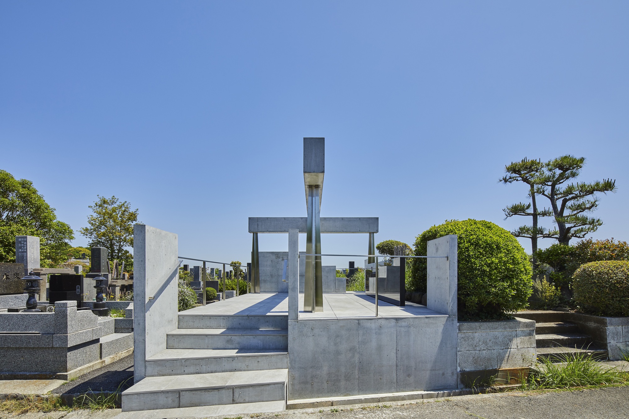 Concrete memorial platform with vertical columns supporting horizontal beams framing a glass monument under clear blue sky