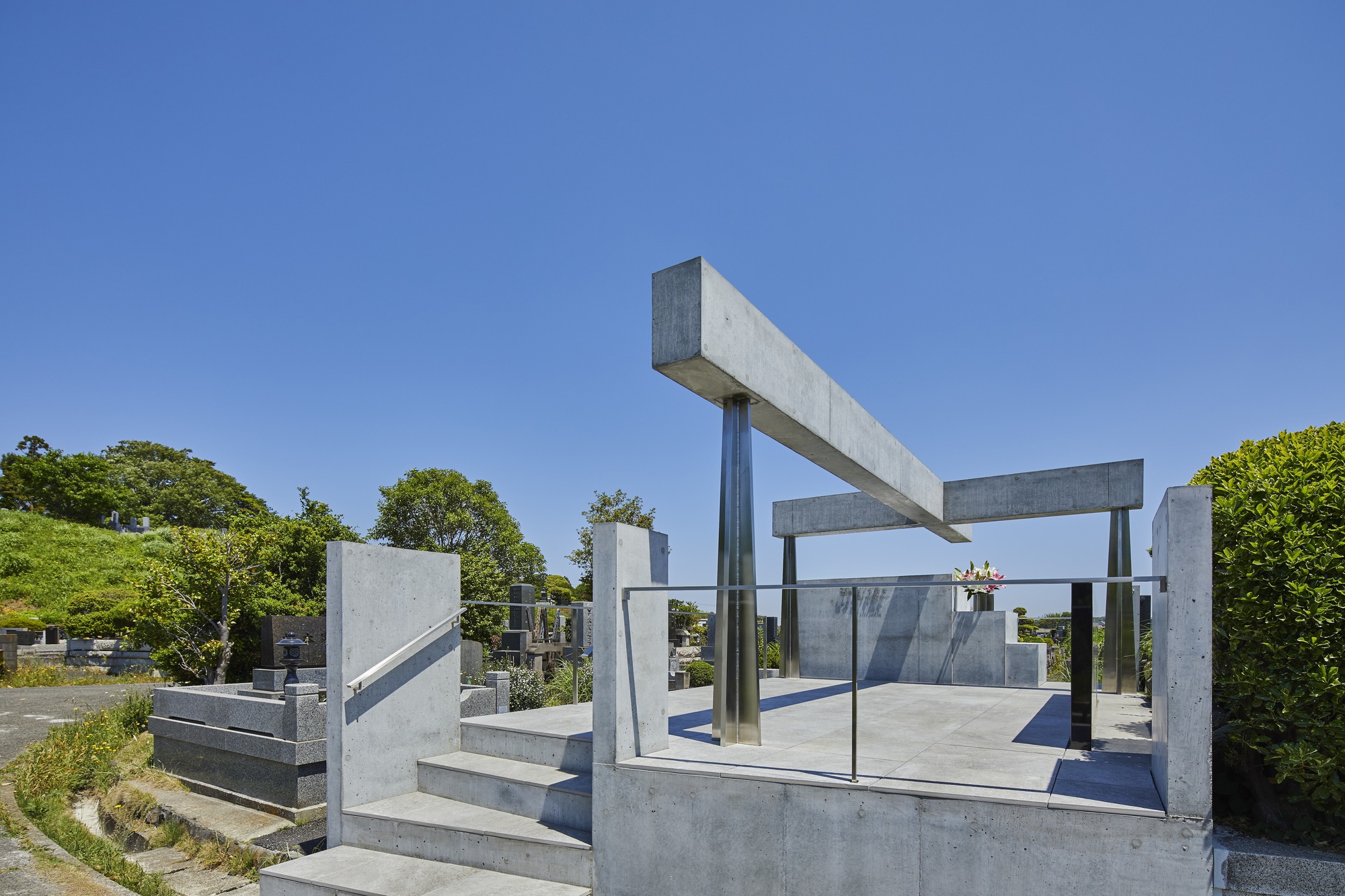 Corner perspective of the stepped concrete base and cantilevered beam structure with glass enclosure among cemetery plots