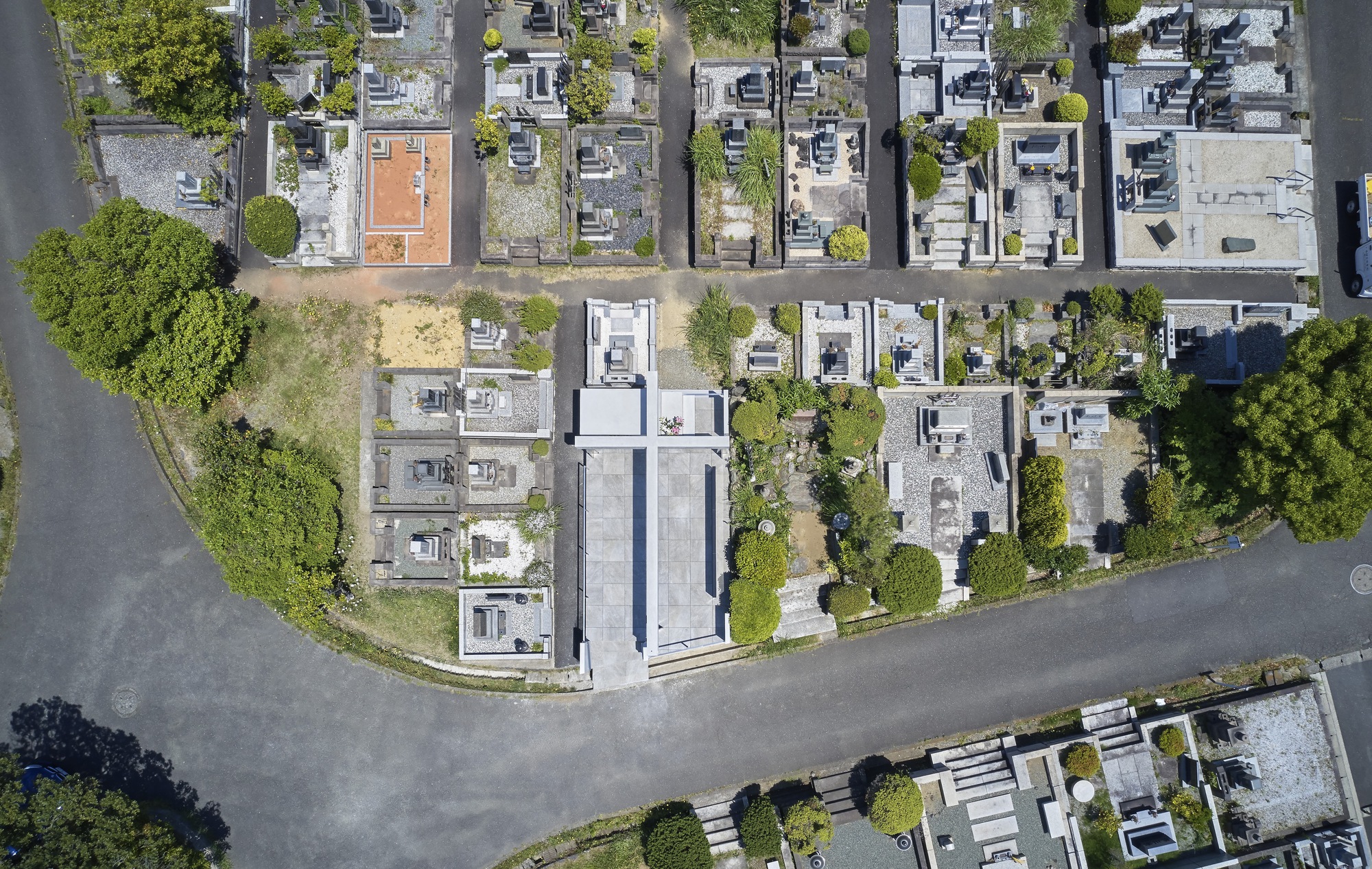 Aerial view of the cruciform concrete memorial centered within its rectangular plot at a curved cemetery road junction