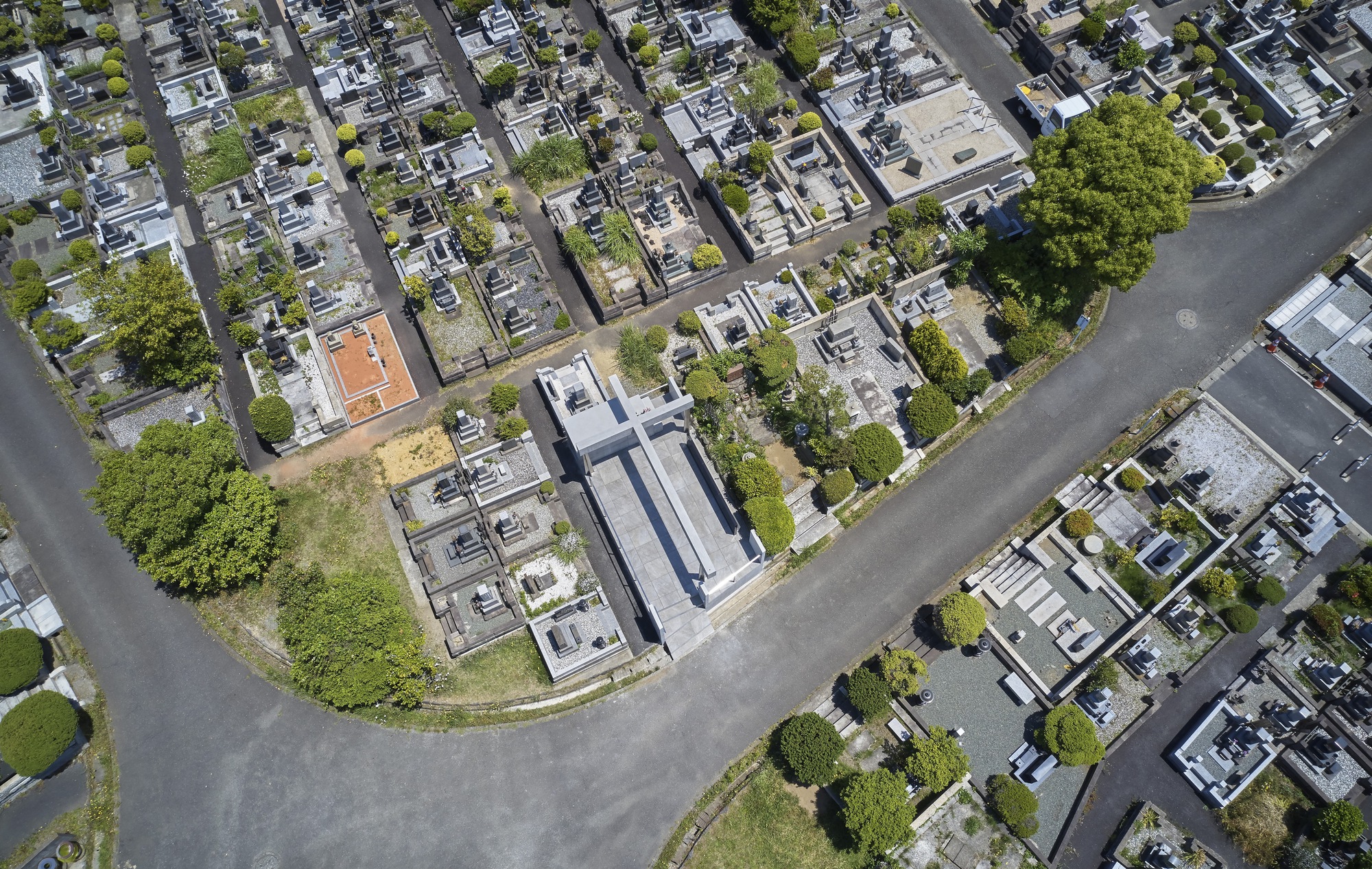 Drone perspective showing the memorial's linear axis aligned with surrounding burial plots and asphalt pathways between green plantings