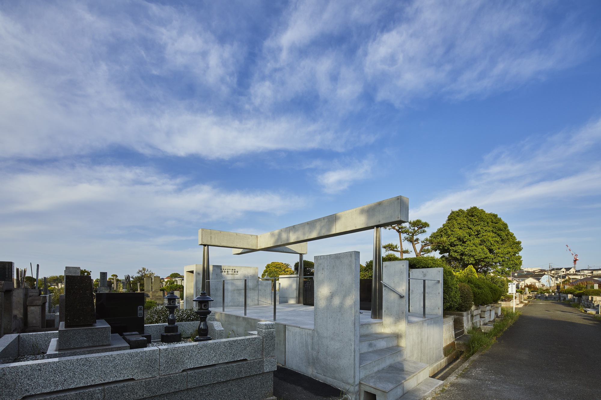 Concrete memorial structure with elevated beam and steel columns among cemetery plots under afternoon sky