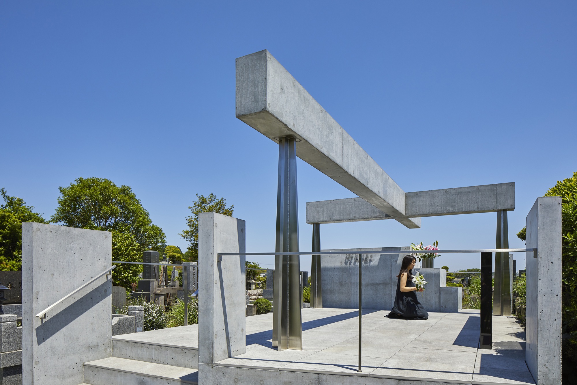 Person kneeling on concrete platform beneath intersecting beams and steel columns with glass balustrade