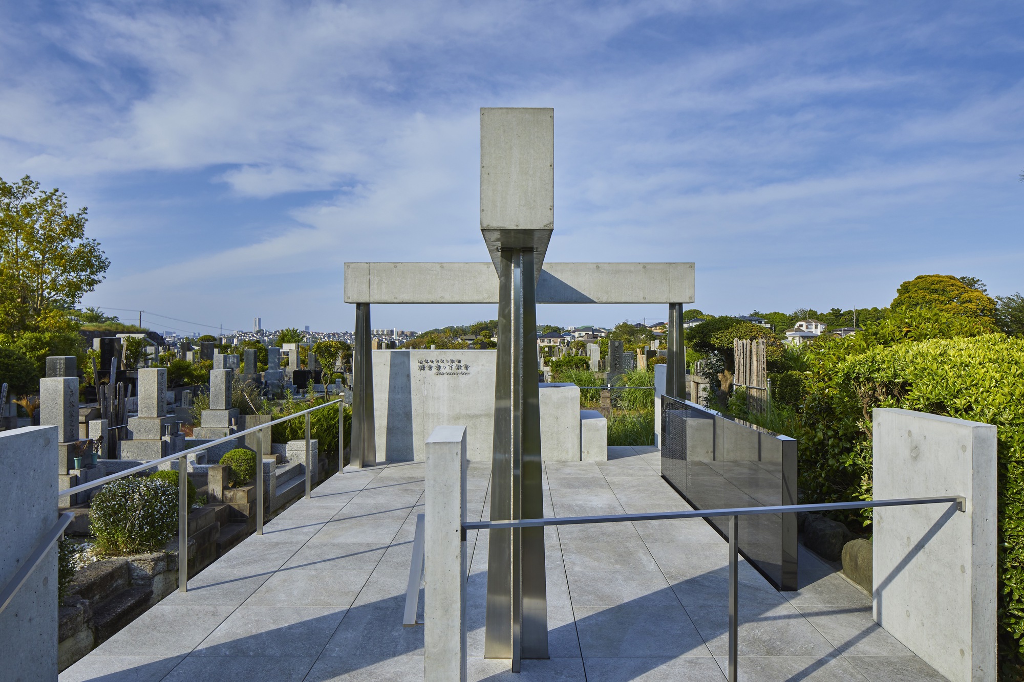 Concrete cross-shaped structure with steel columns and central monument stone overlooking cemetery landscape