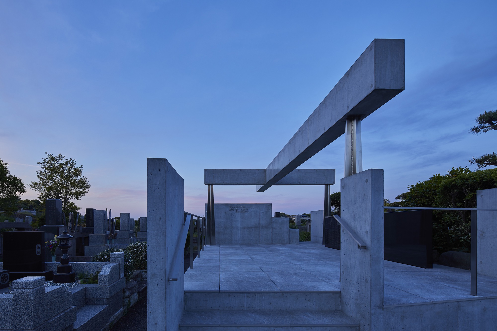Concrete pavilion with overhead beam structure photographed at dusk with pink sky behind