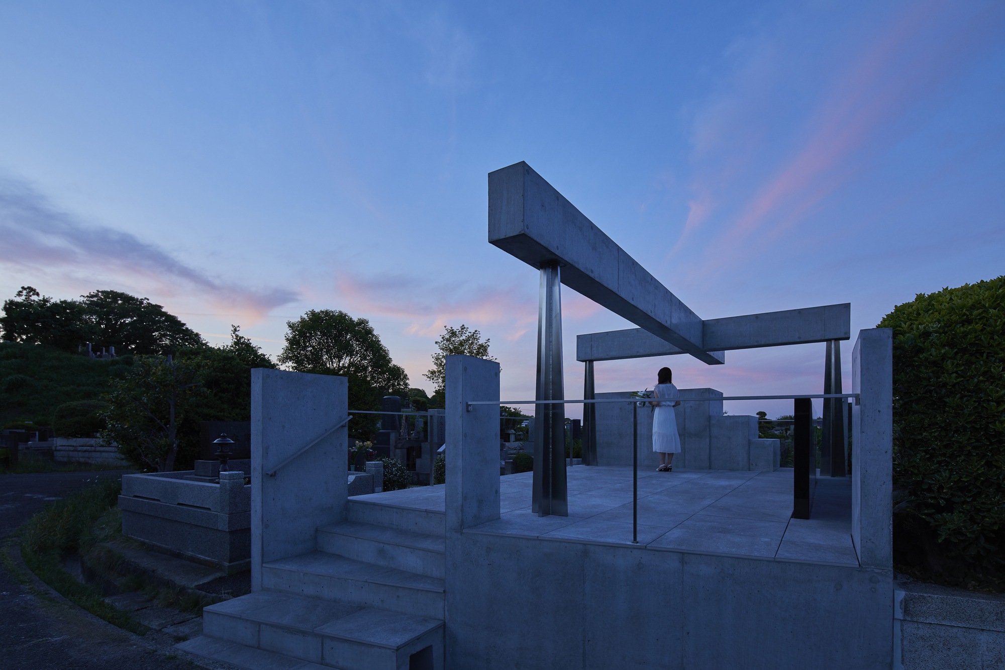 Open concrete platform with columns and beams as a figure stands beneath at twilight
