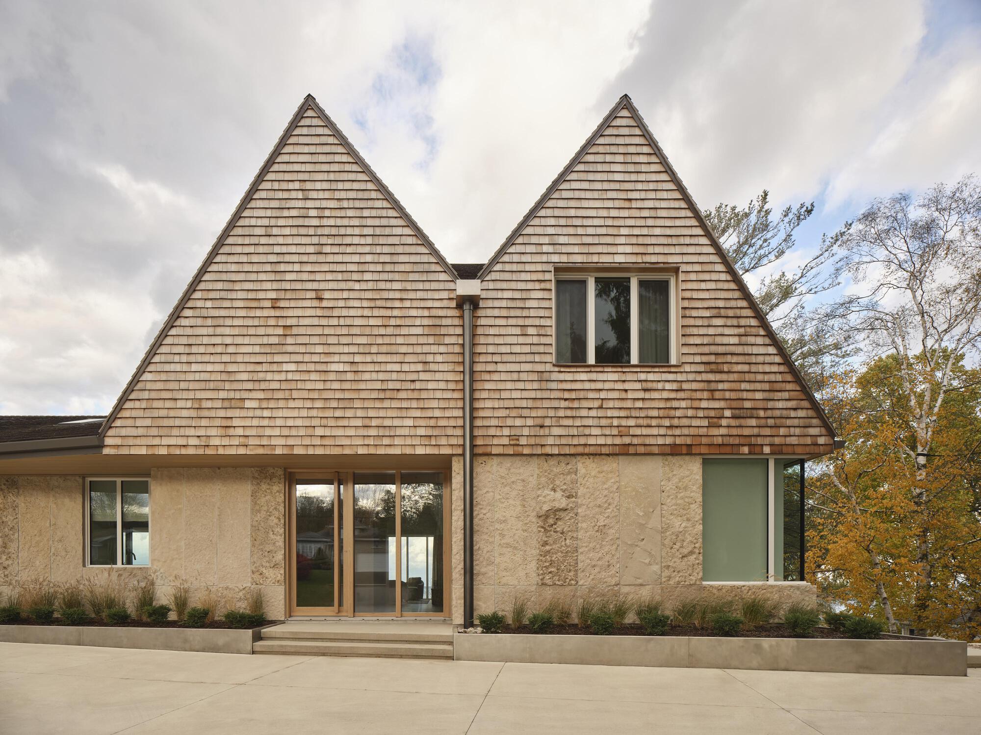 Entrance facade with twin gabled cedar shingle roofs above rammed earth walls and concrete terrace