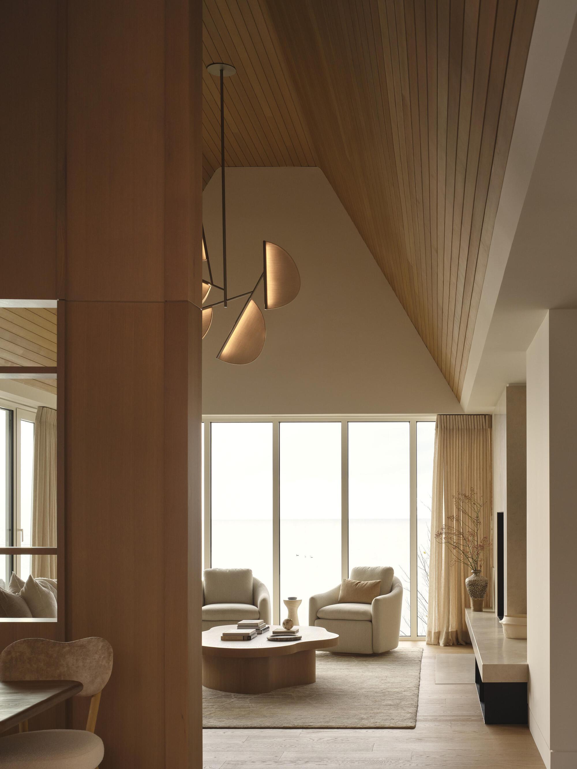 Living room with vaulted timber ceiling and pendant lighting above seating area facing tall windows