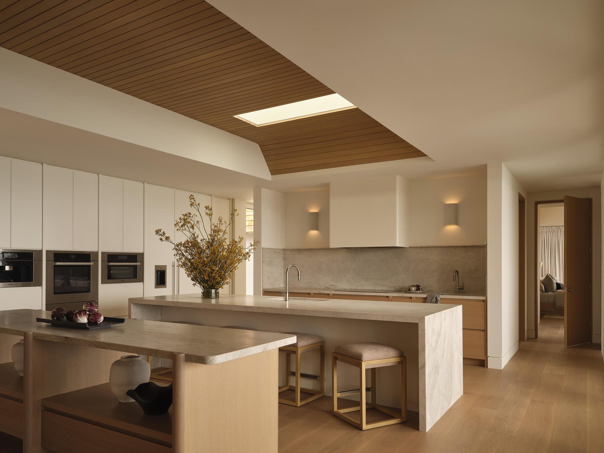 Kitchen with timber ceiling panels, central island, and integrated dining table under skylight