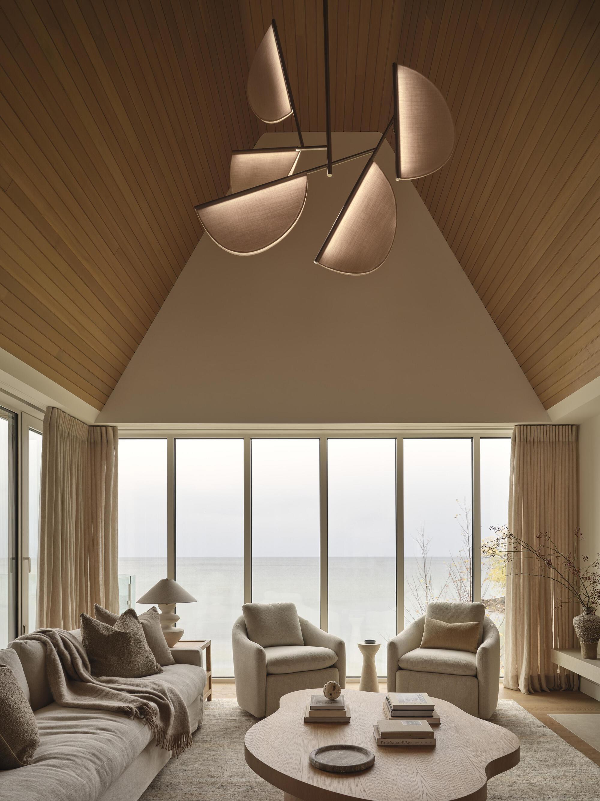 Living room with vaulted timber ceiling and glazed wall overlooking the water under overcast skies