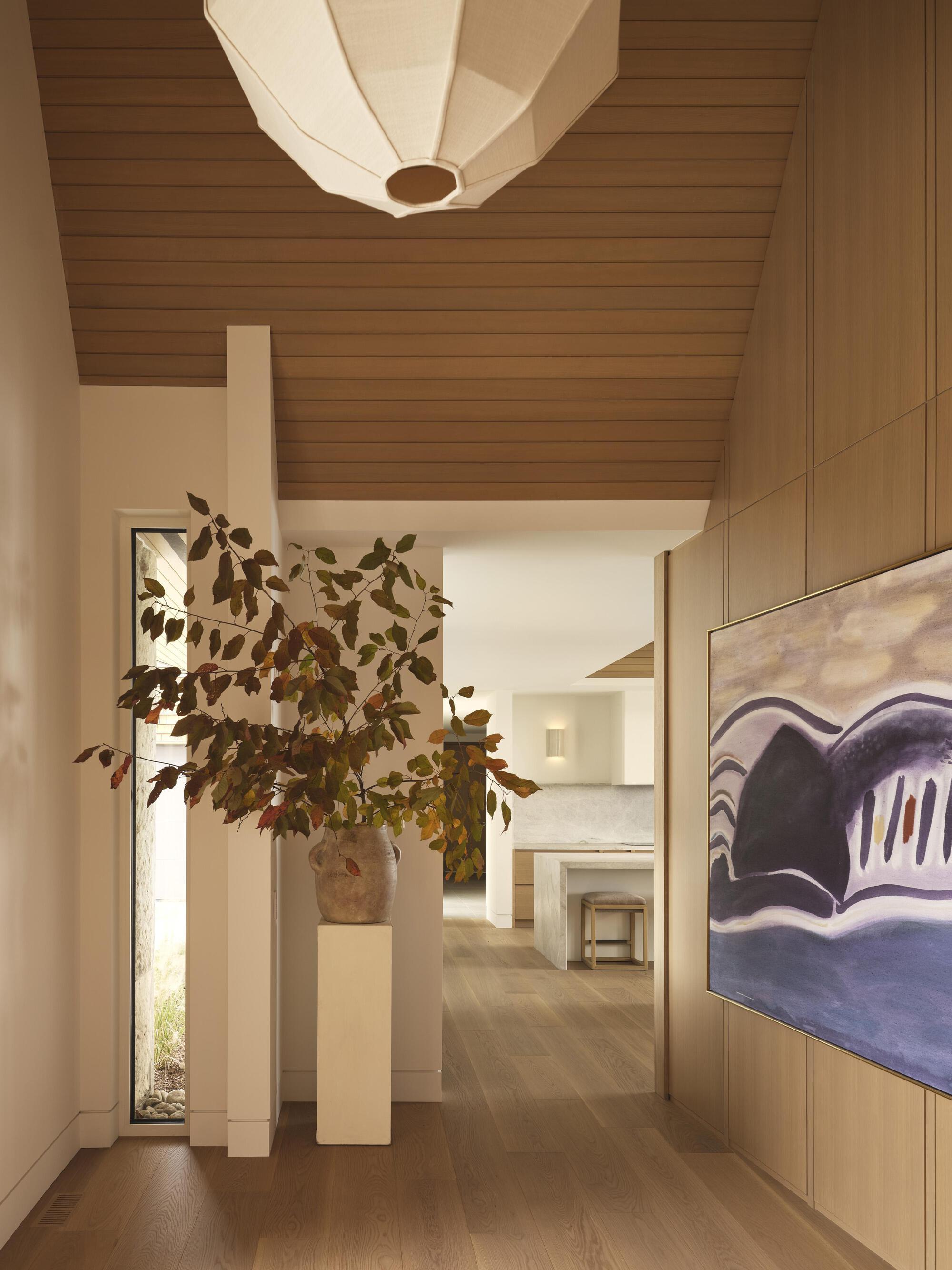 Hallway with horizontal wood ceiling and sculptural pendant light above a branching arrangement in terracotta vessel