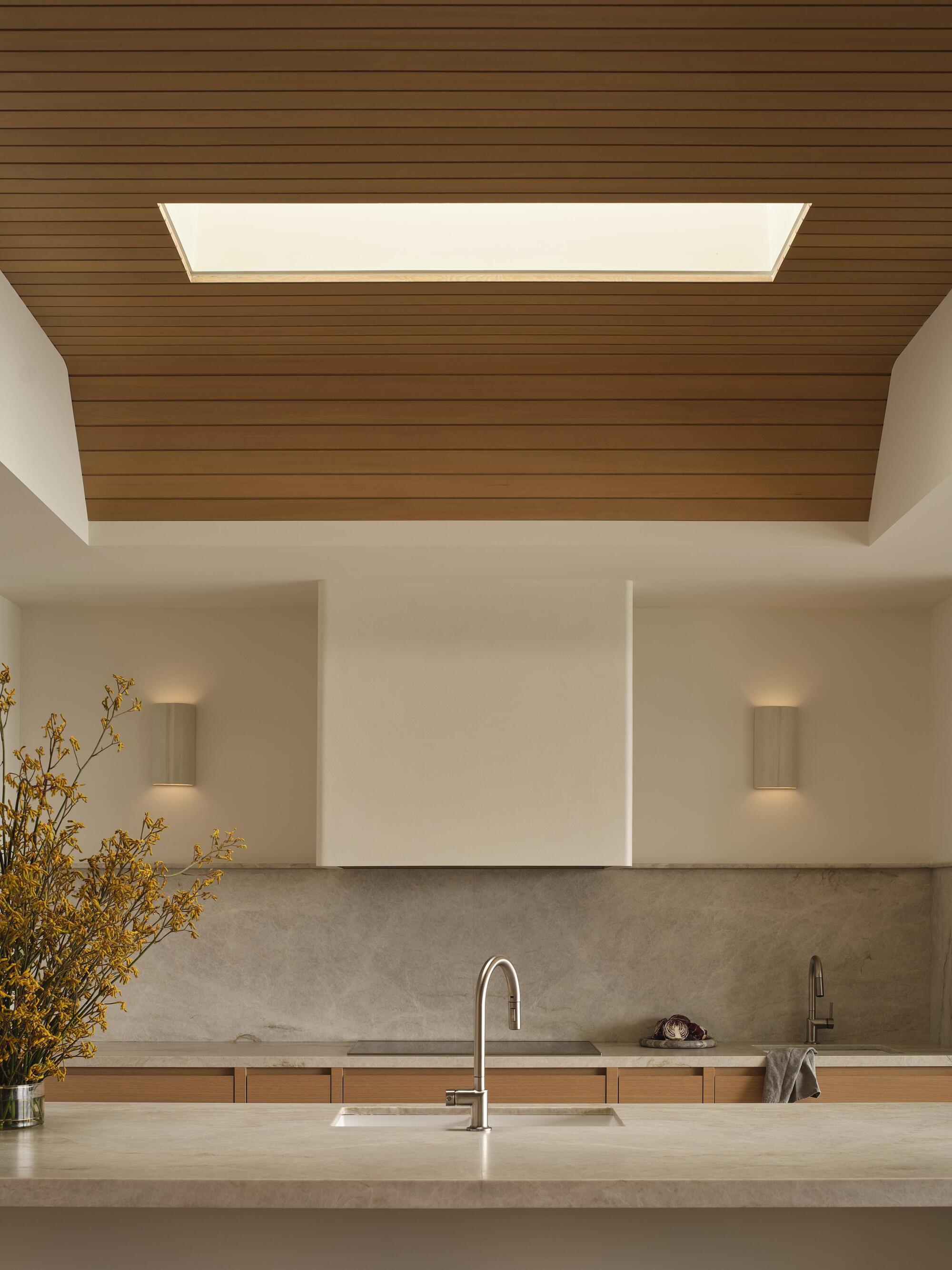 Kitchen island with stone countertop under a timber ceiling panel with integrated skylight