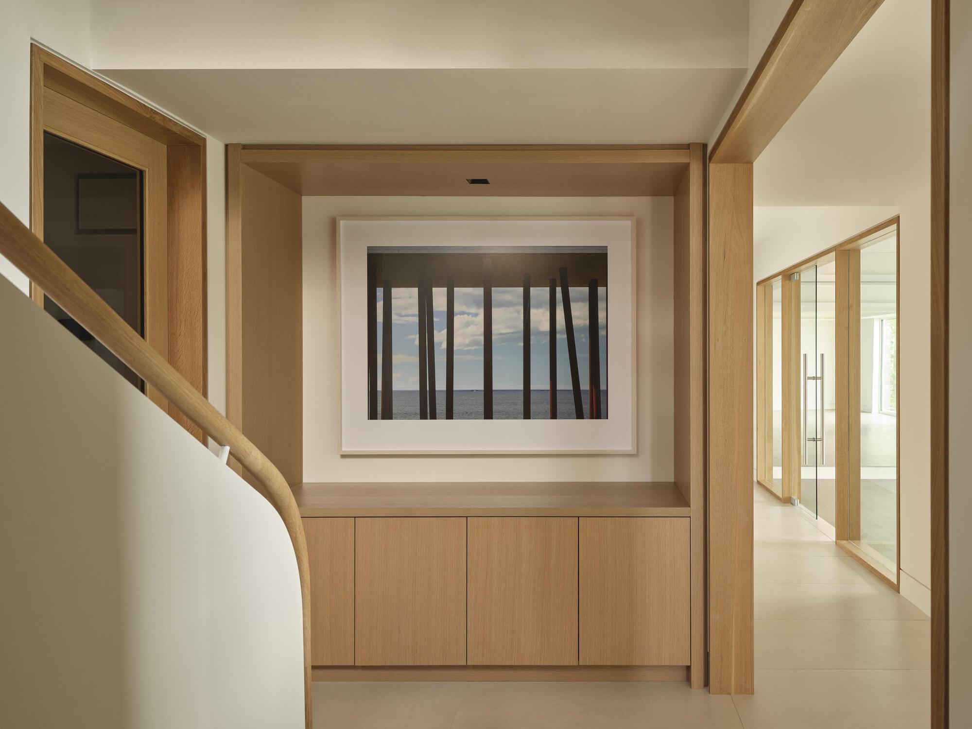 Light oak corridor with timber-framed window opening and built-in cabinets beneath a curved stairwell