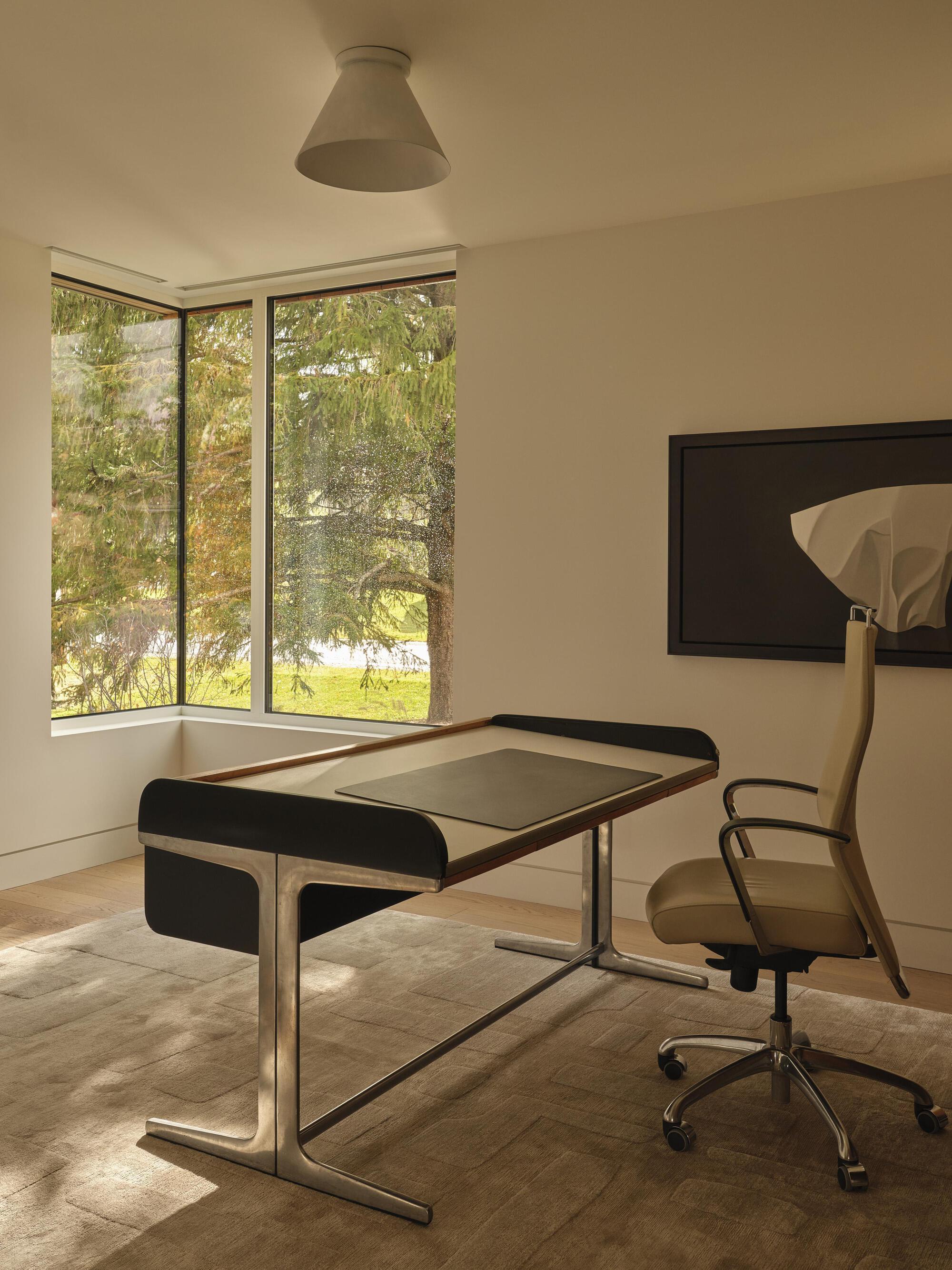 Corner study with black-framed desk and tall window overlooking trees in afternoon light