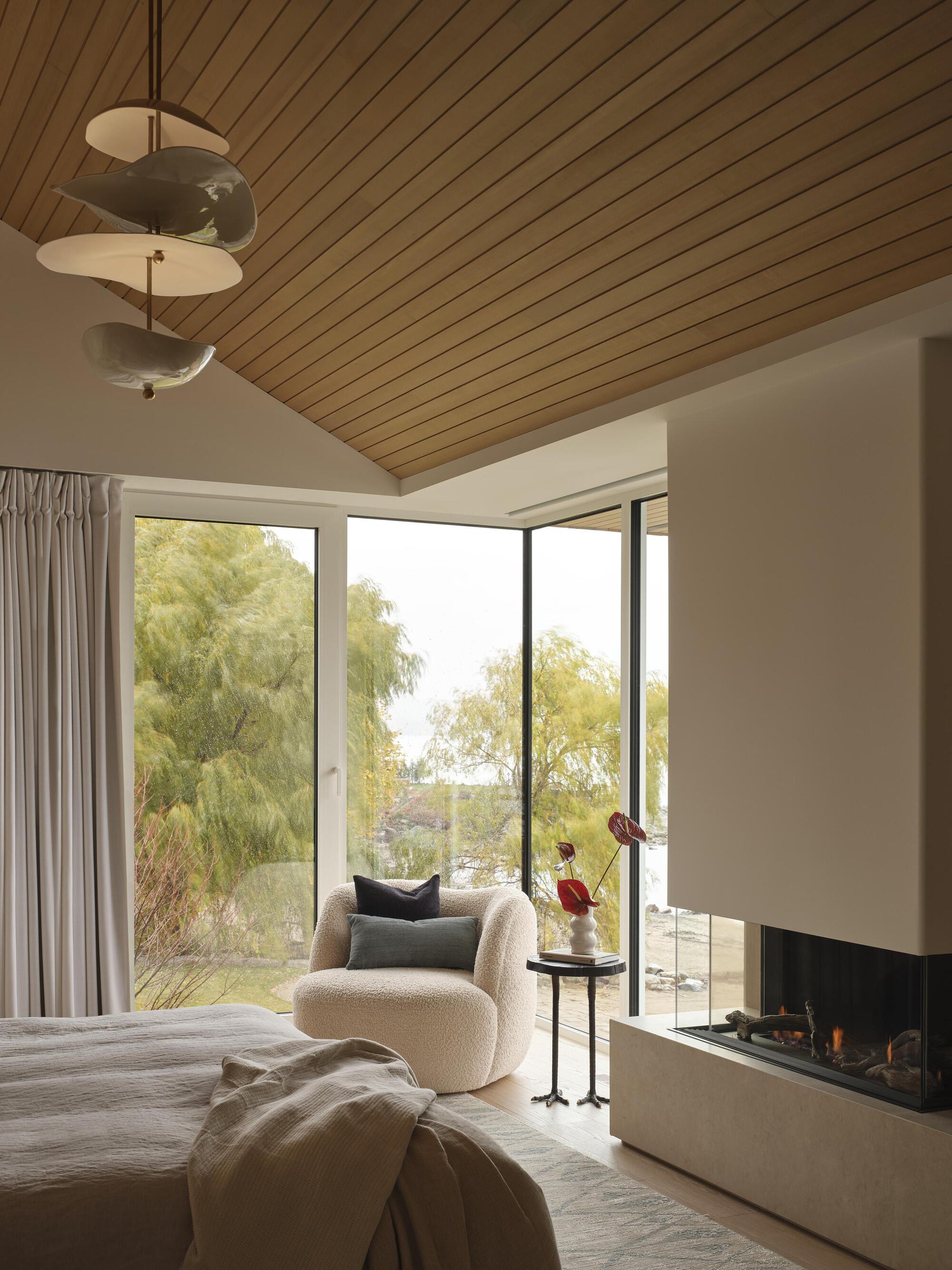 Bedroom with timber slat ceiling and corner glazing opening to garden foliage and fireplace