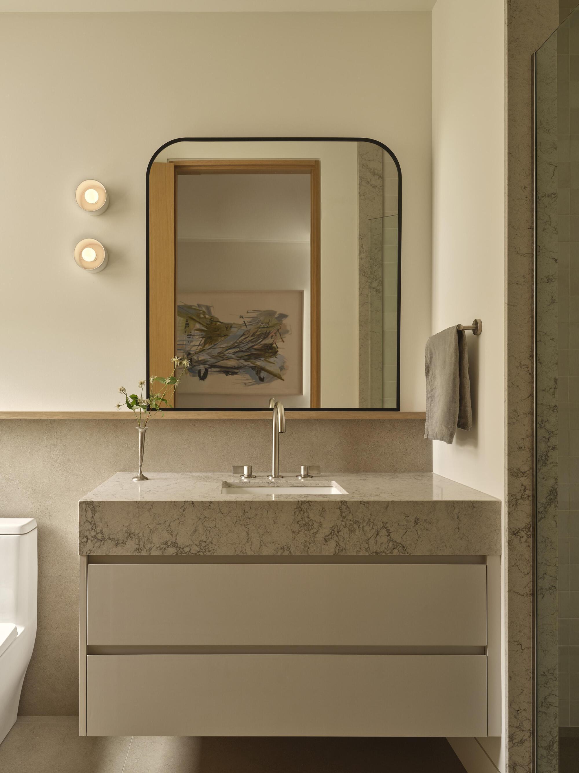 Floating vanity with thick stone countertop beneath a rounded-corner mirror and two circular wall sconces