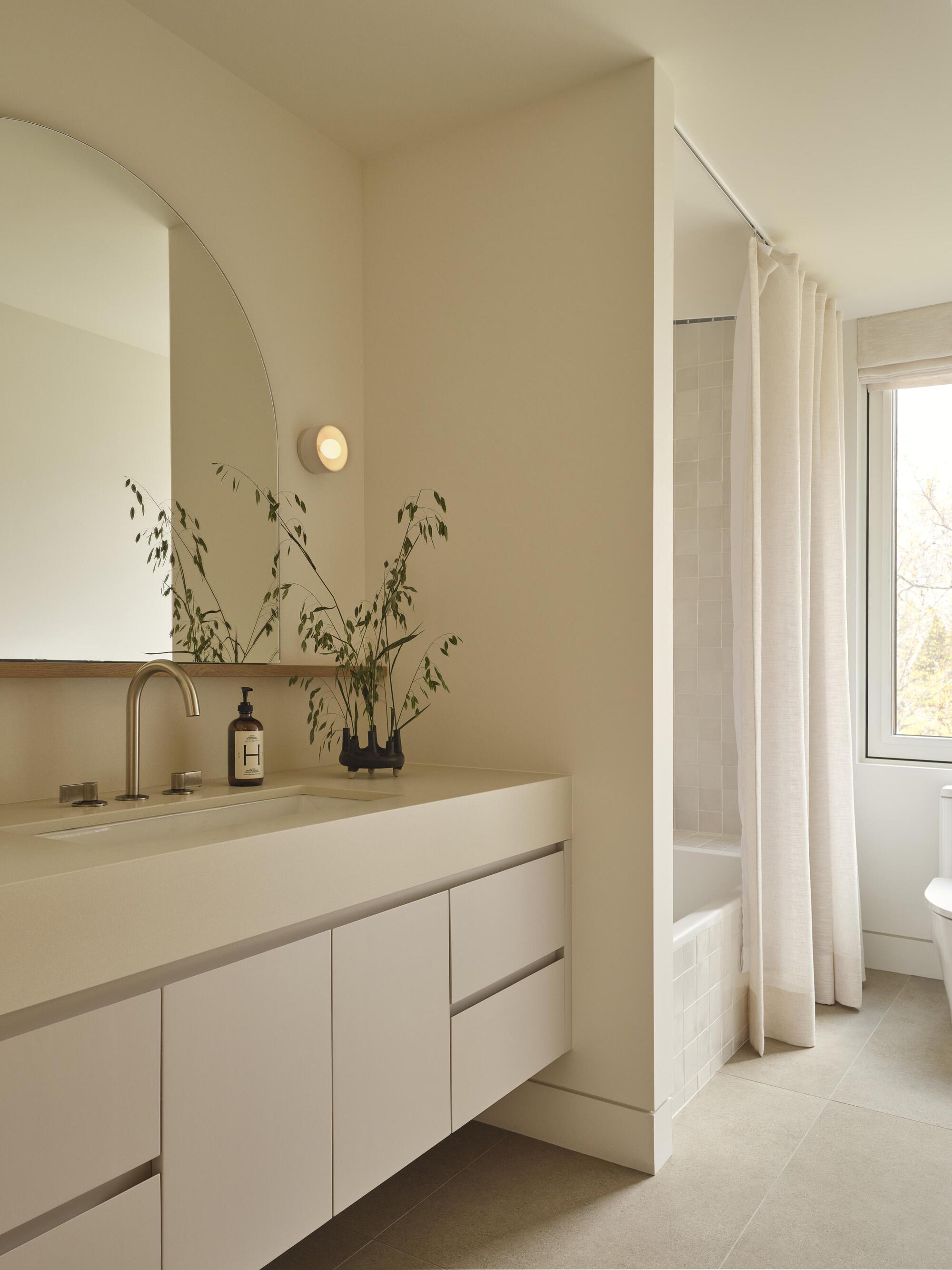 Bathroom vanity with arched mirror and dried grasses in a vase beside the window