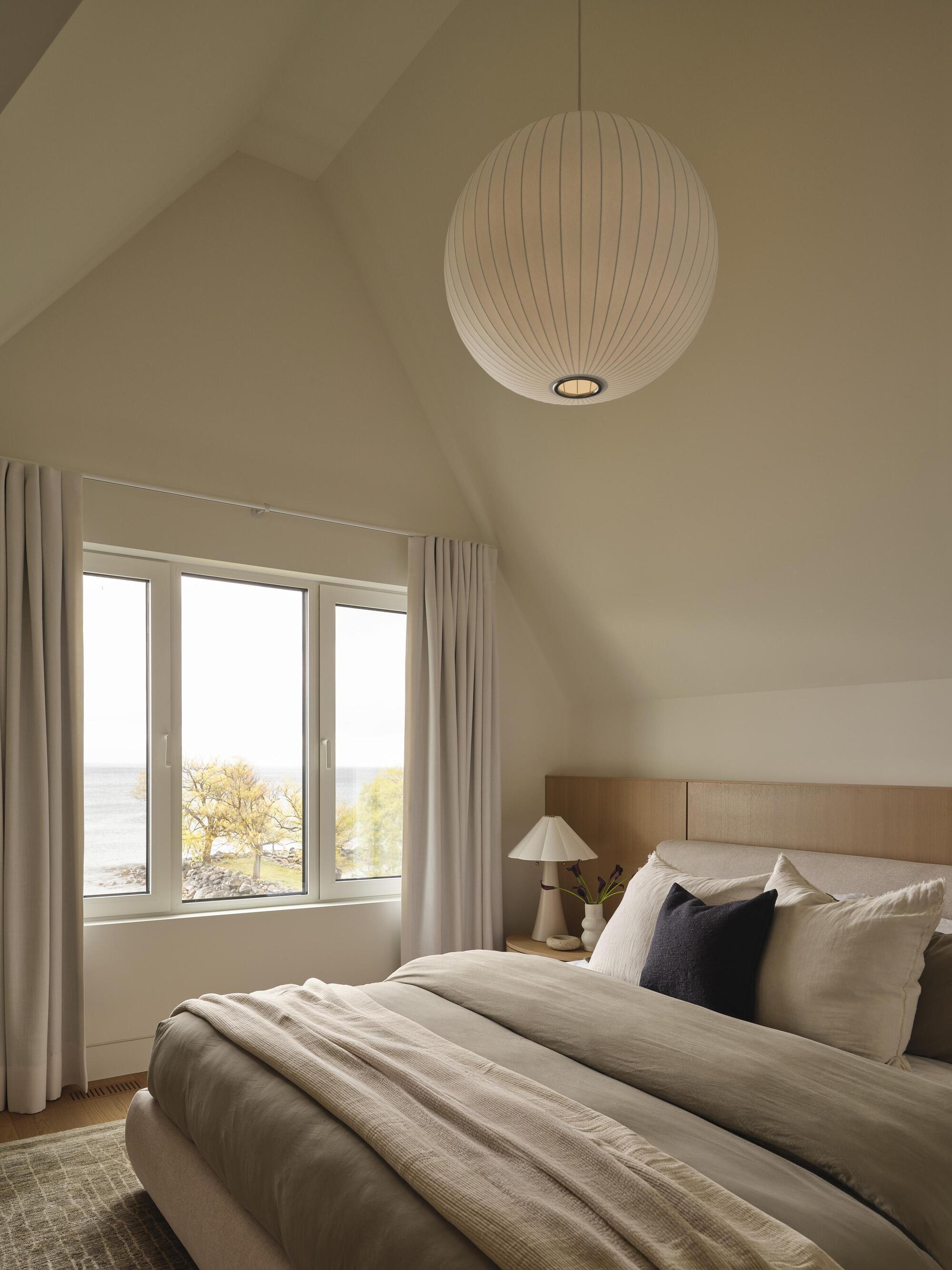 Bedroom with vaulted ceiling and spherical pendant light above a window overlooking the water