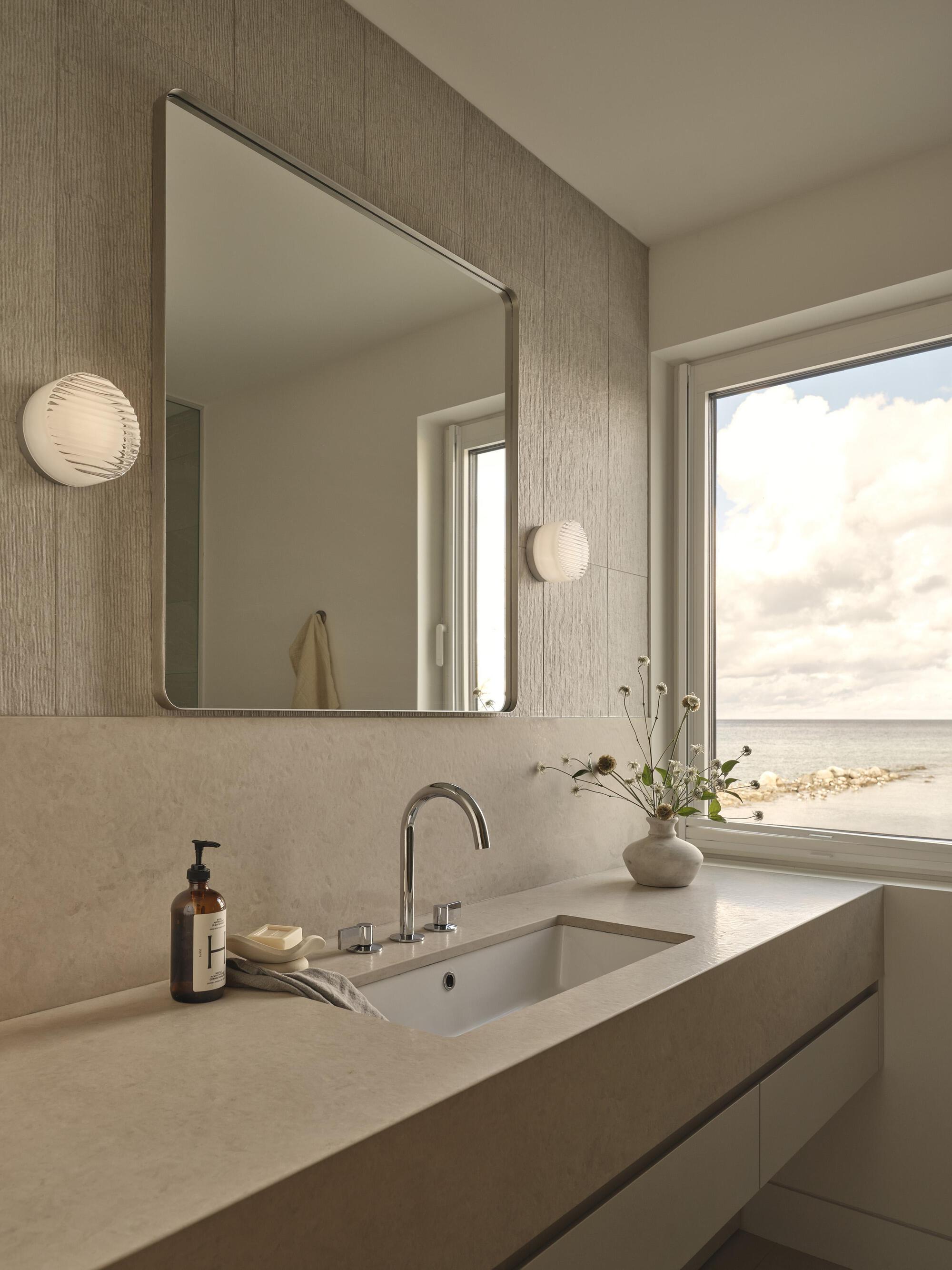 Vanity counter with textured wall panel and square mirror reflecting the ocean view window