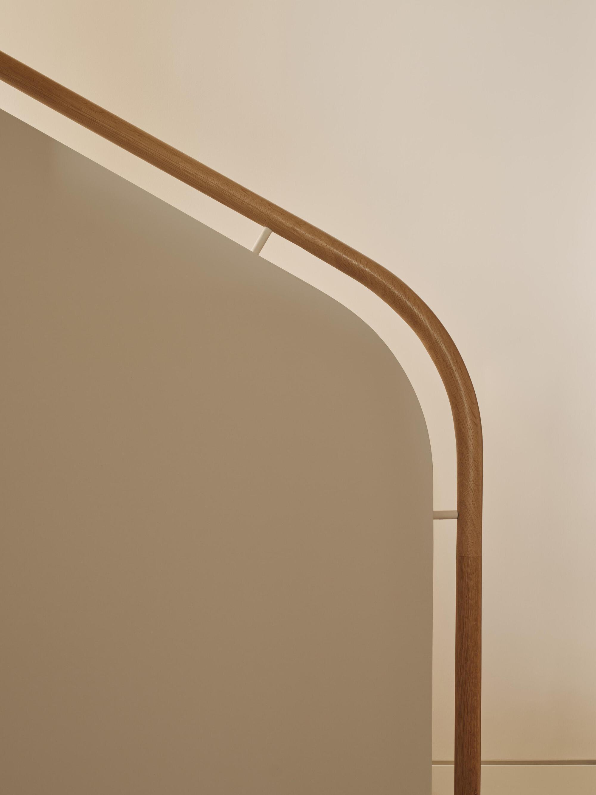 Close-up of the rounded timber handrail curving along a plastered archway edge