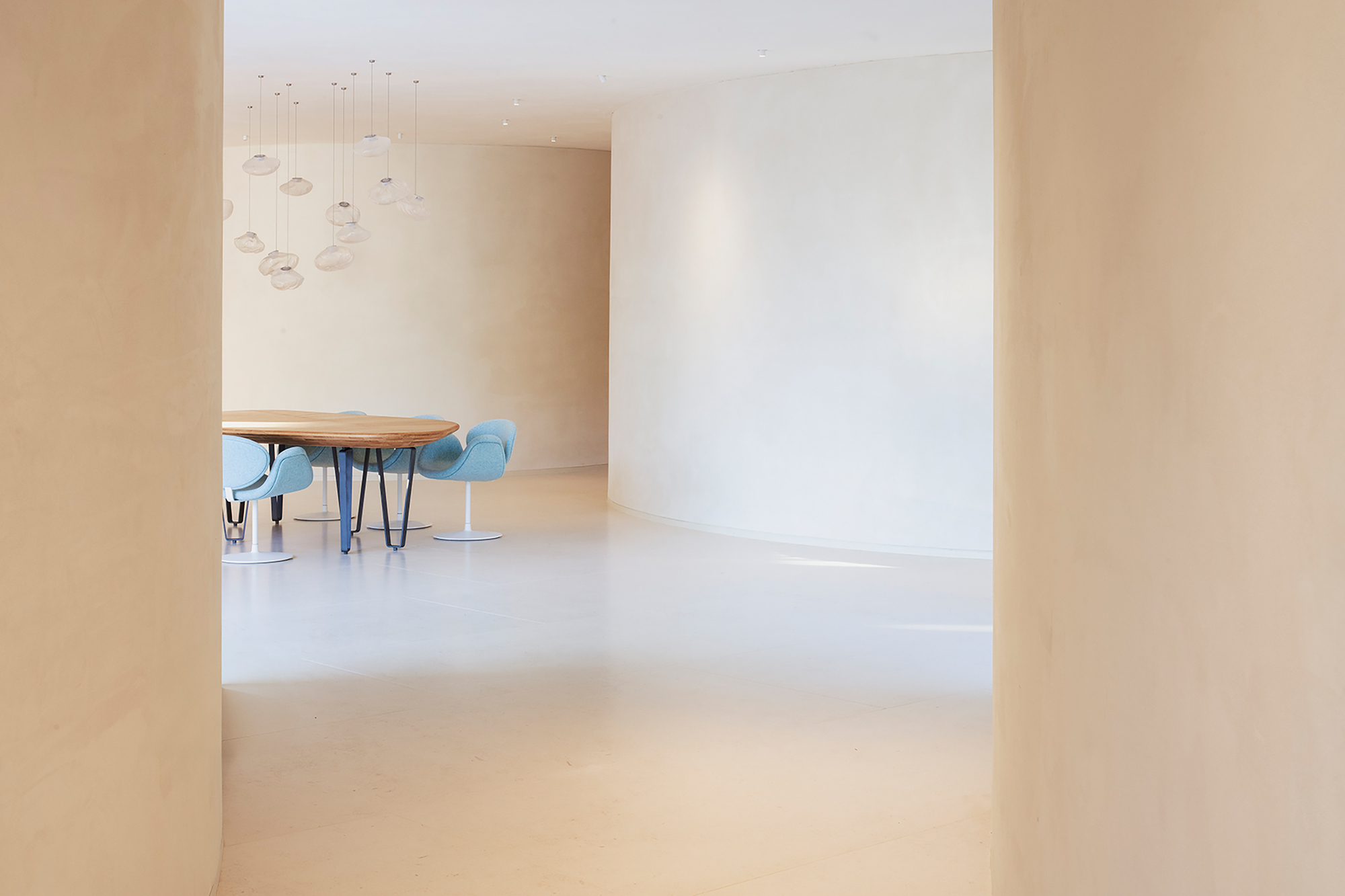 View through curved opening to dining area with pale plaster walls and polished floor