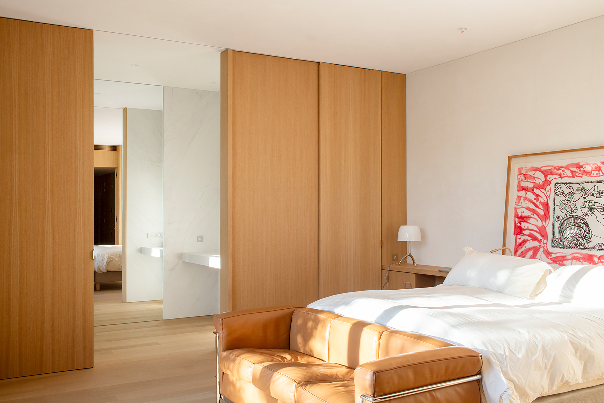 Bedroom with oak wardrobe panels, white bedding, and a framed artwork above the nightstand