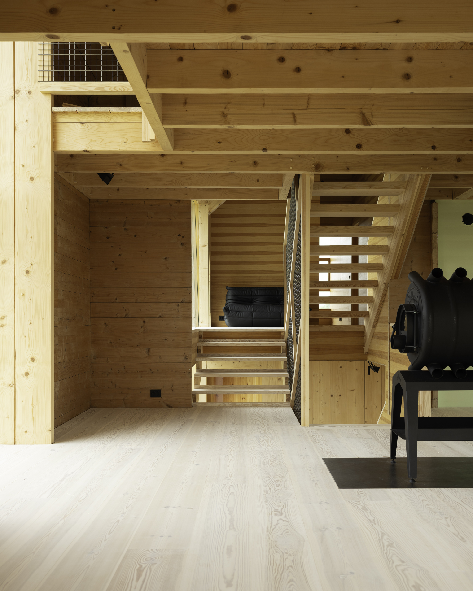 Open-tread timber staircase ascending between plank-clad walls and exposed ceiling joists