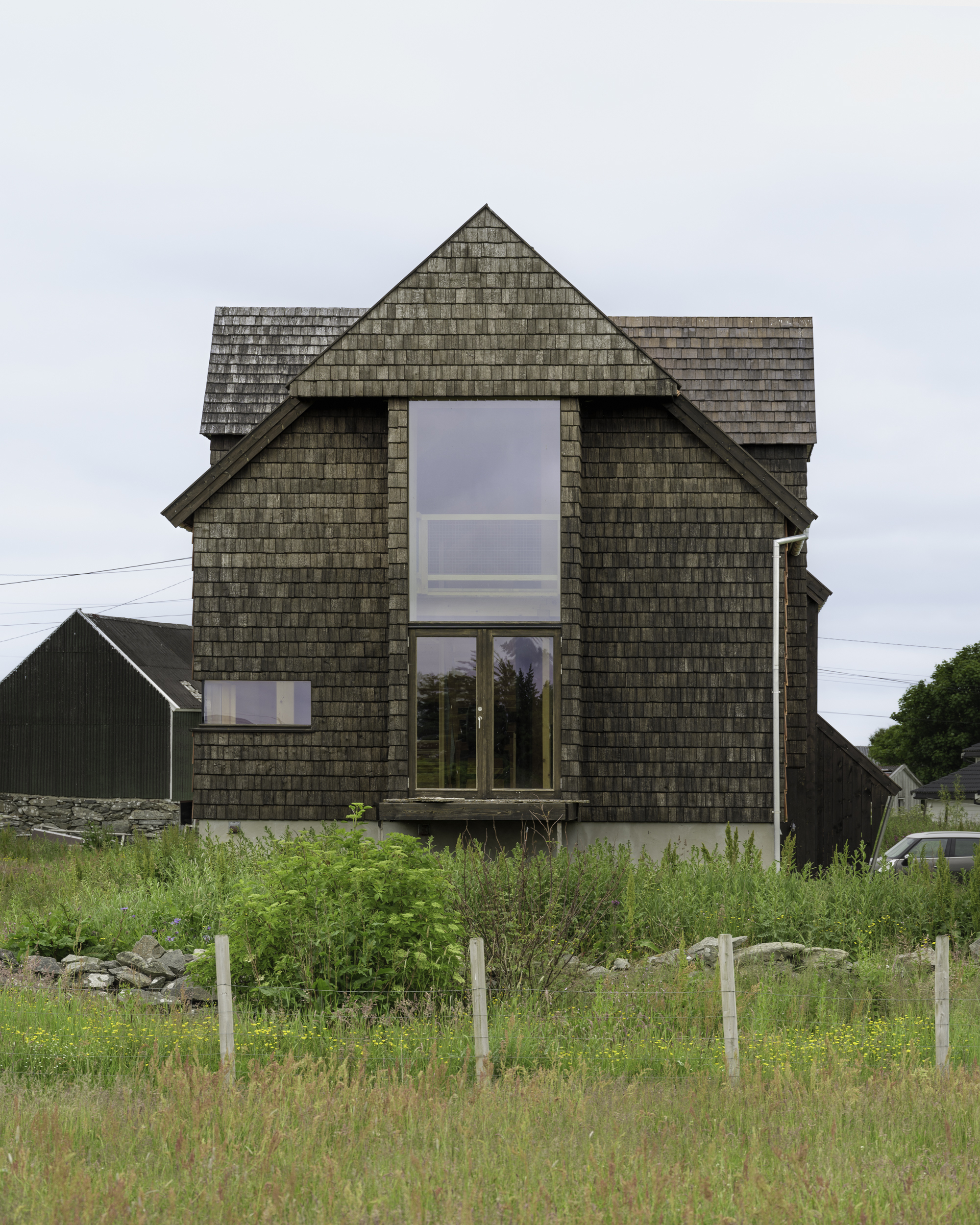 Front gable facade clad in dark shingles with a tall window overlooking grasses