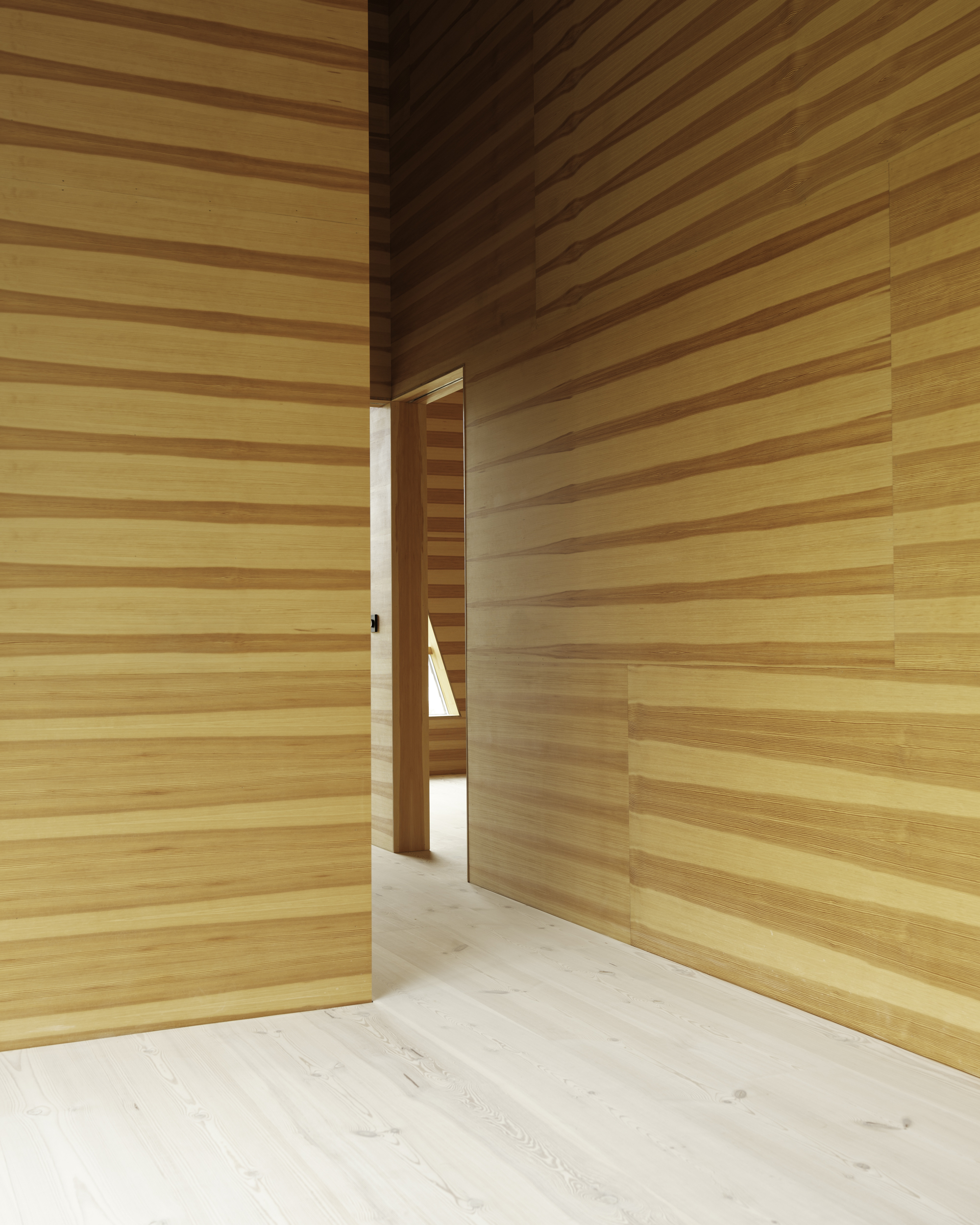 Narrow doorway framing a passage through horizontal timber clad walls in warm natural light