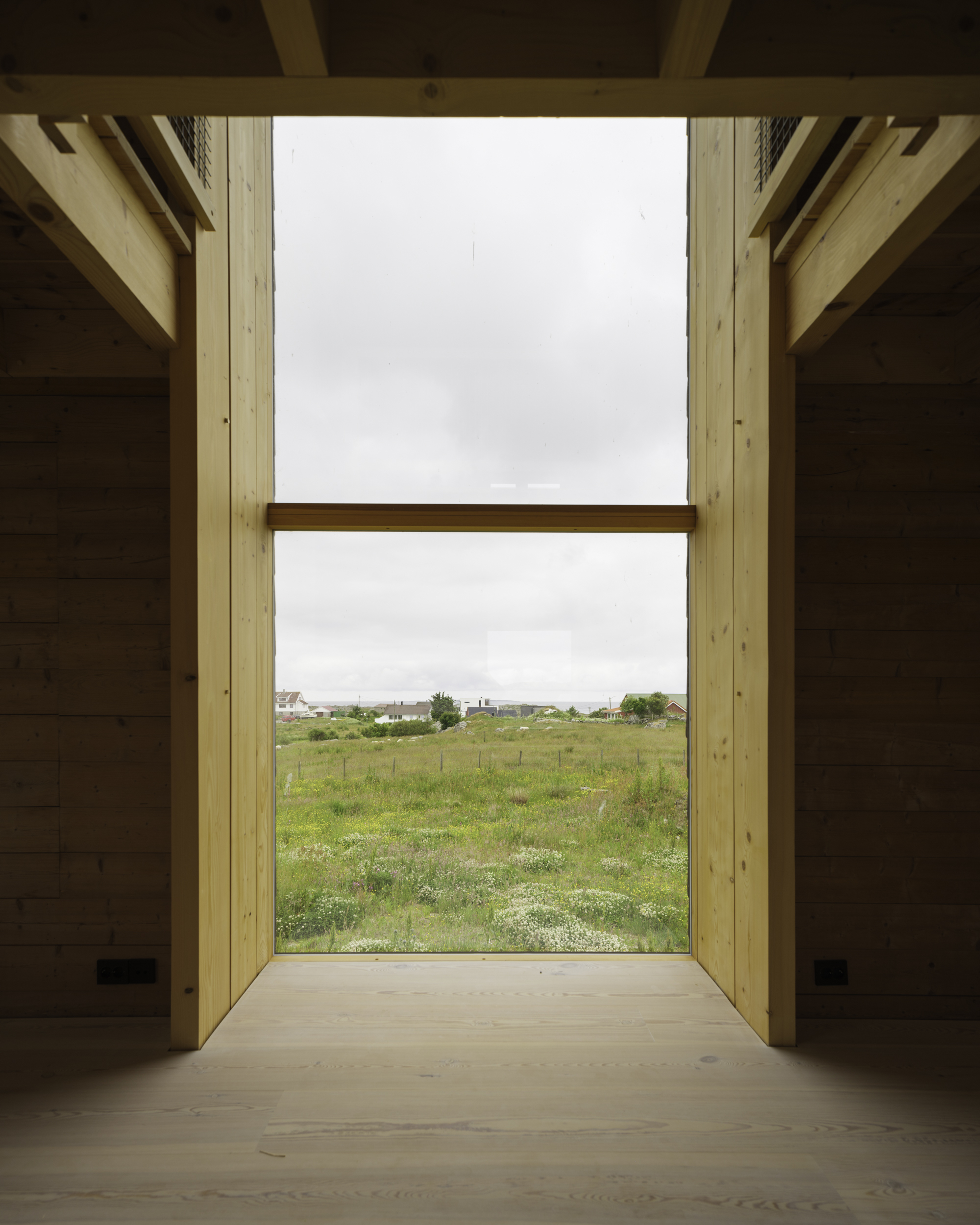 Floor-to-ceiling window framing view of green field with scattered houses under overcast sky