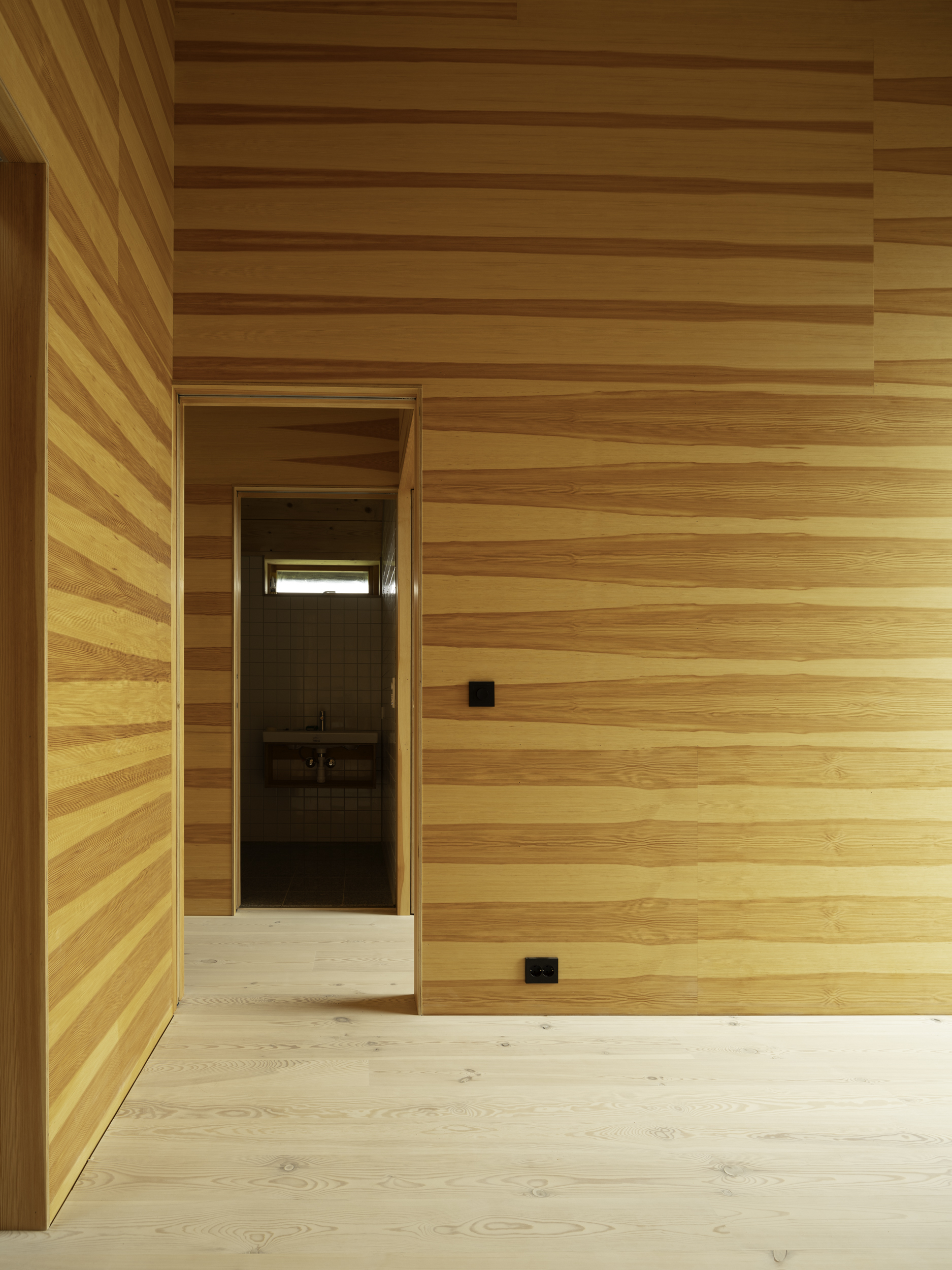 Interior corner with horizontal timber wall cladding and doorway leading to darker room beyond