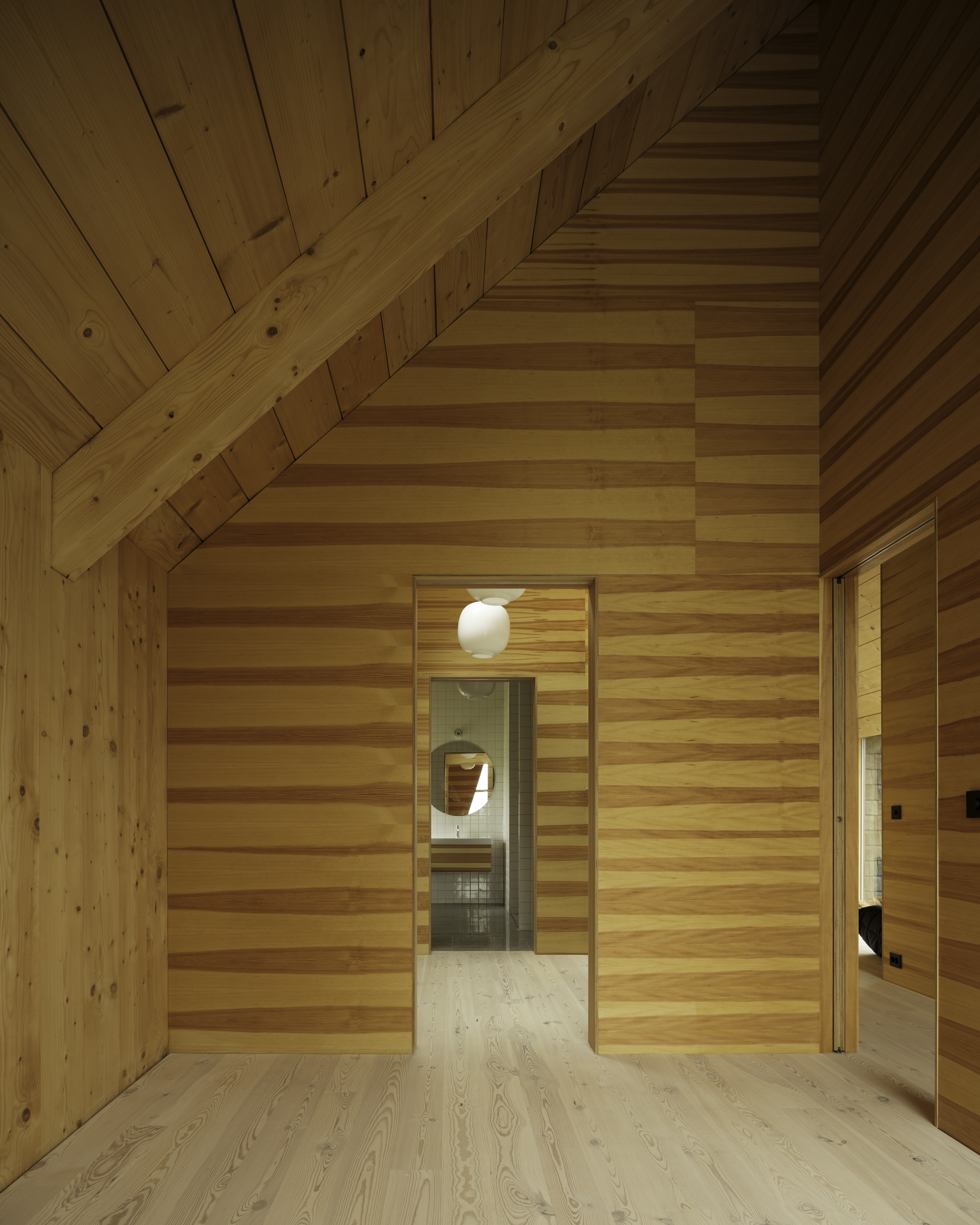 Gabled ceiling space with horizontal timber cladding and illuminated doorway with spherical pendant light