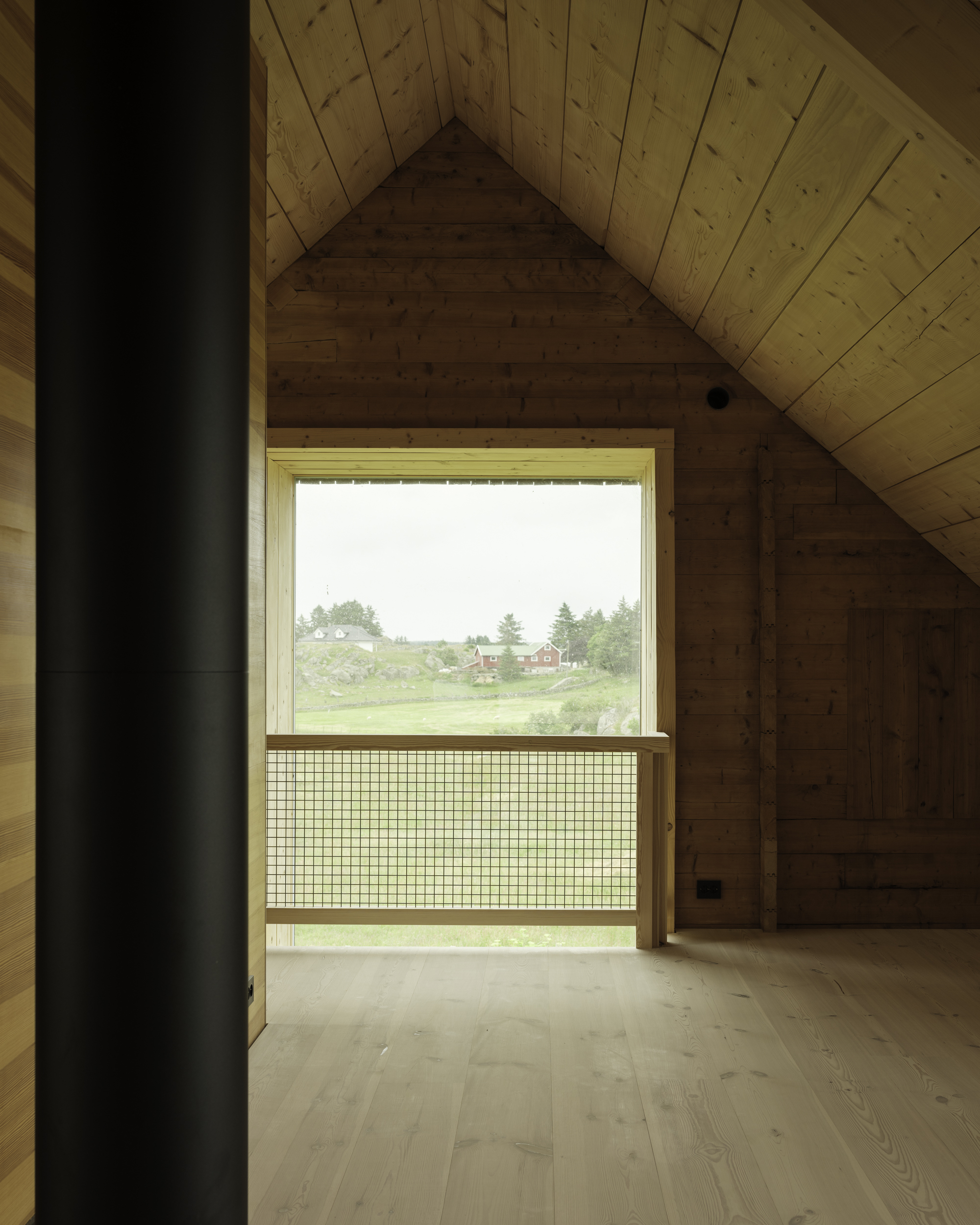 Upper floor timber room with gabled ceiling and mesh safety railing at window overlooking fields