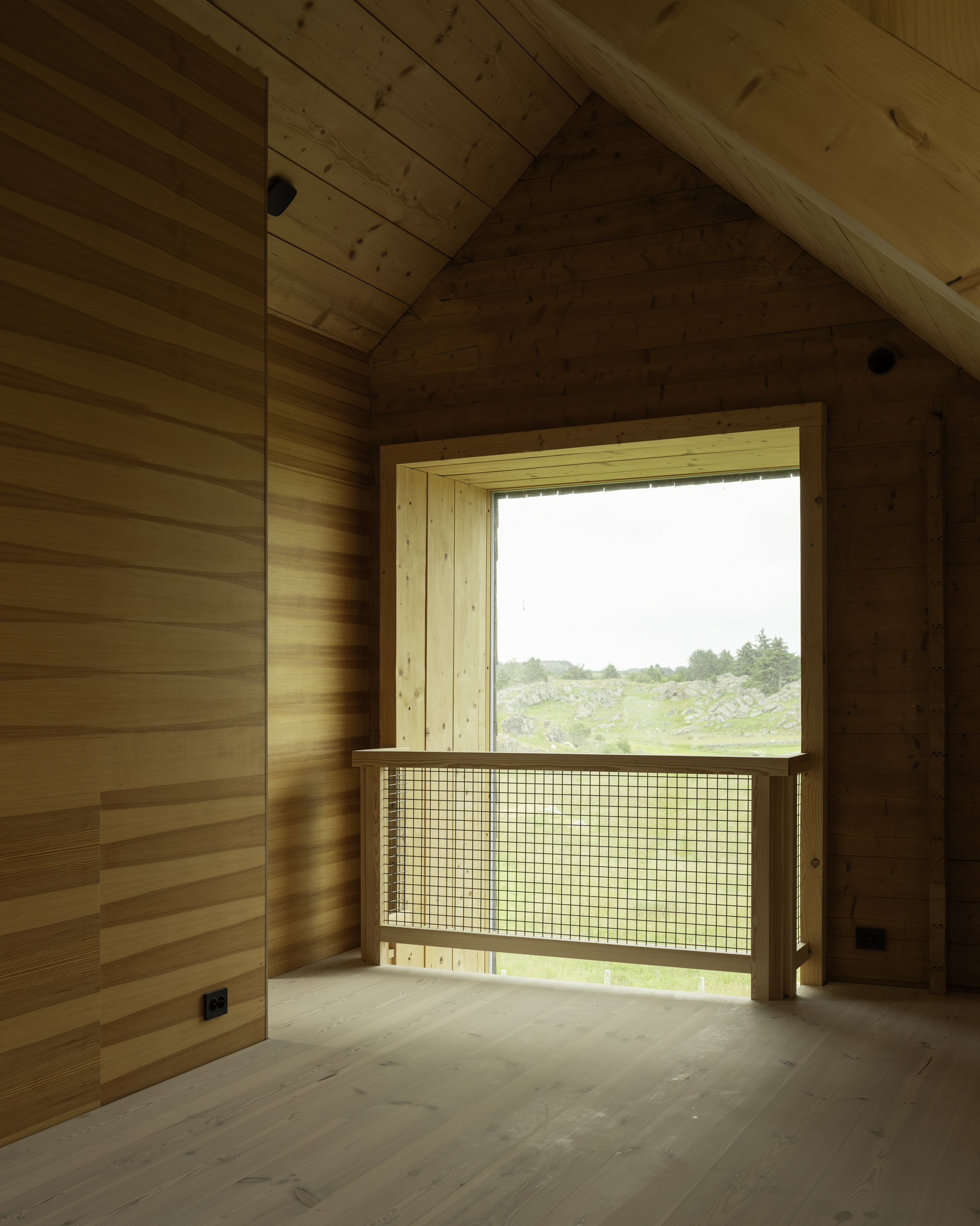 Timber-lined alcove with window featuring mesh guard rail and view to green meadow