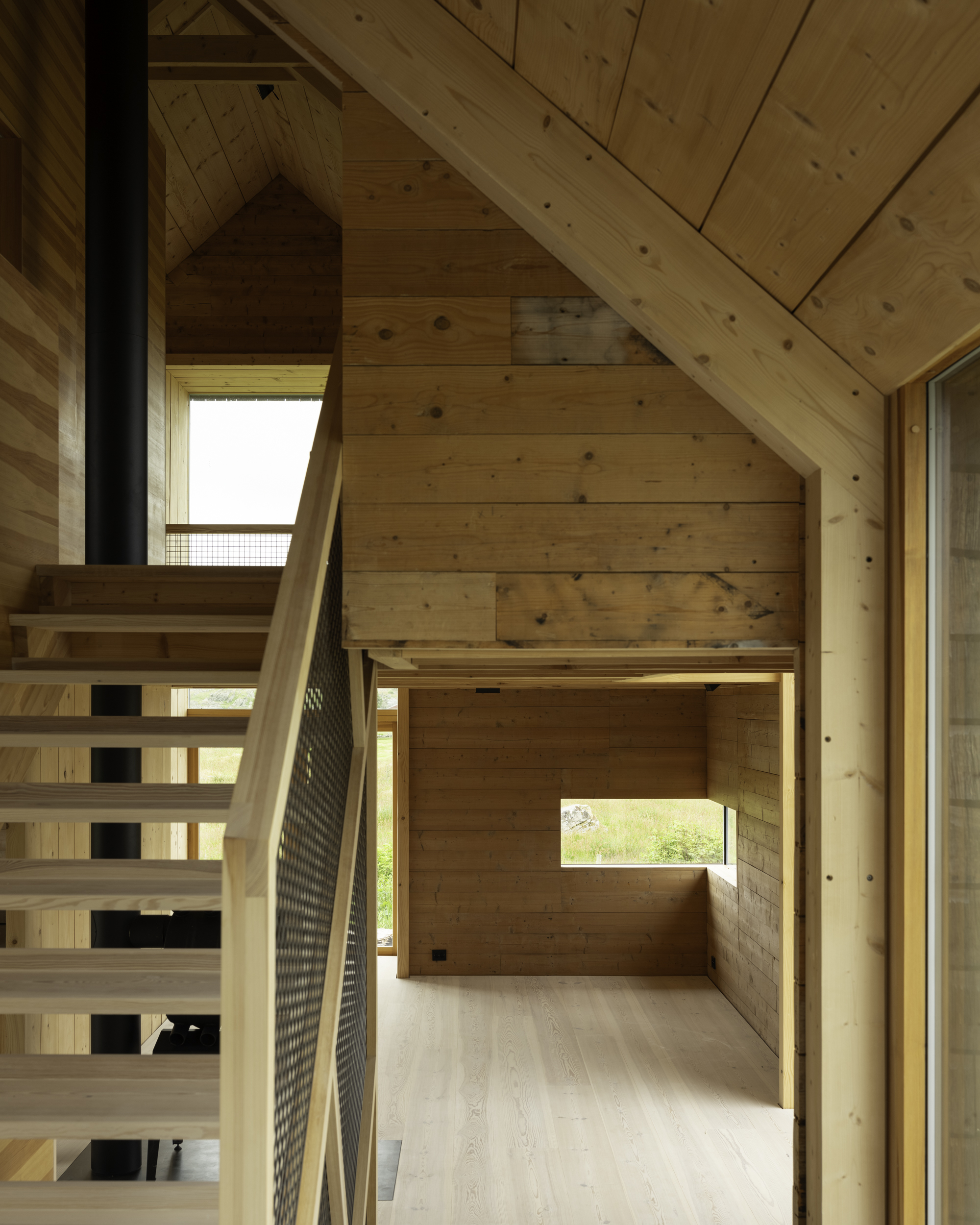 Wood-clad interior showing open stair with metal mesh balustrade beneath a pitched roof with skylights