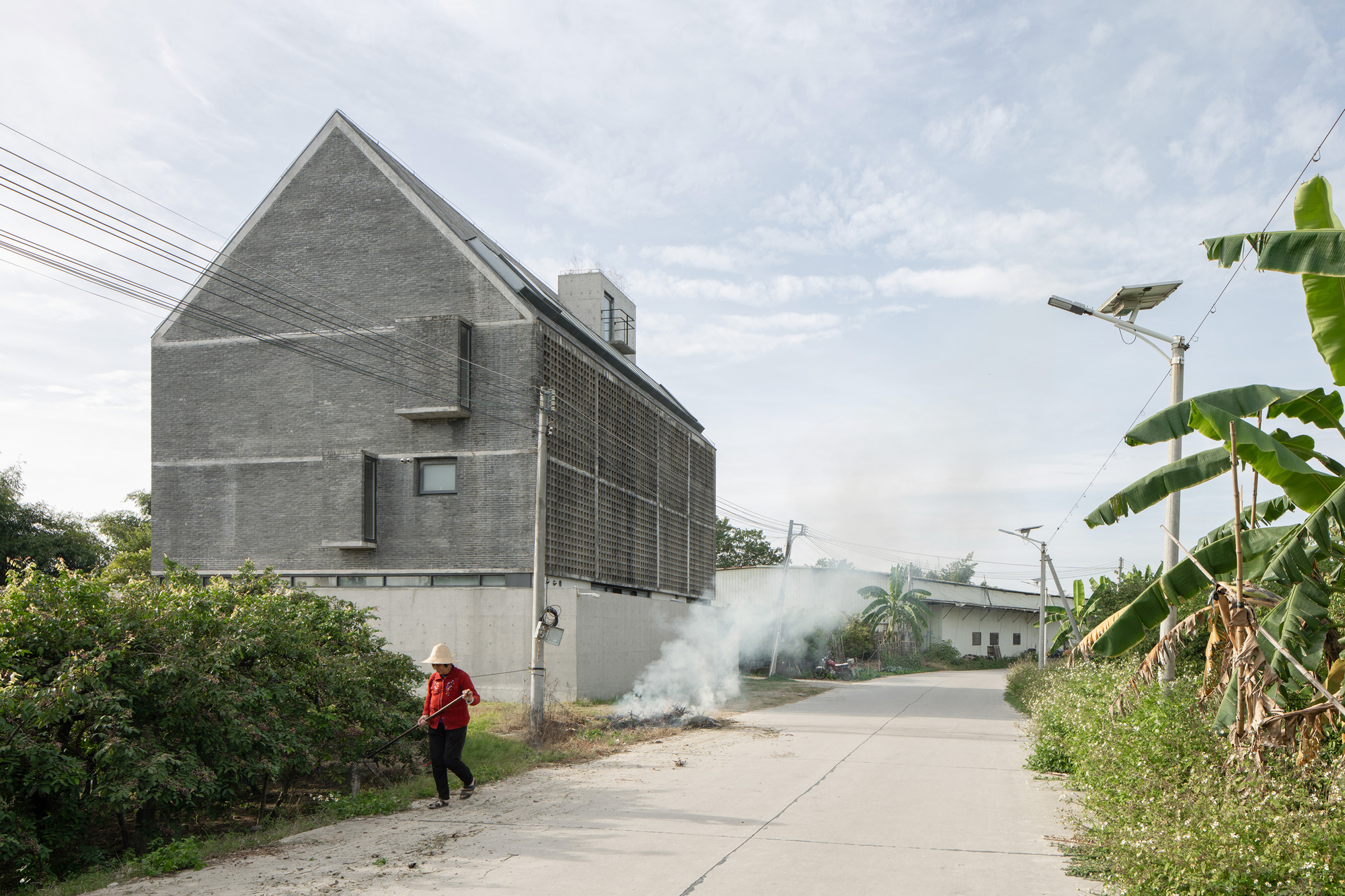 Street view of the house-shaped concrete volume with perforated brick screen and a person walking past