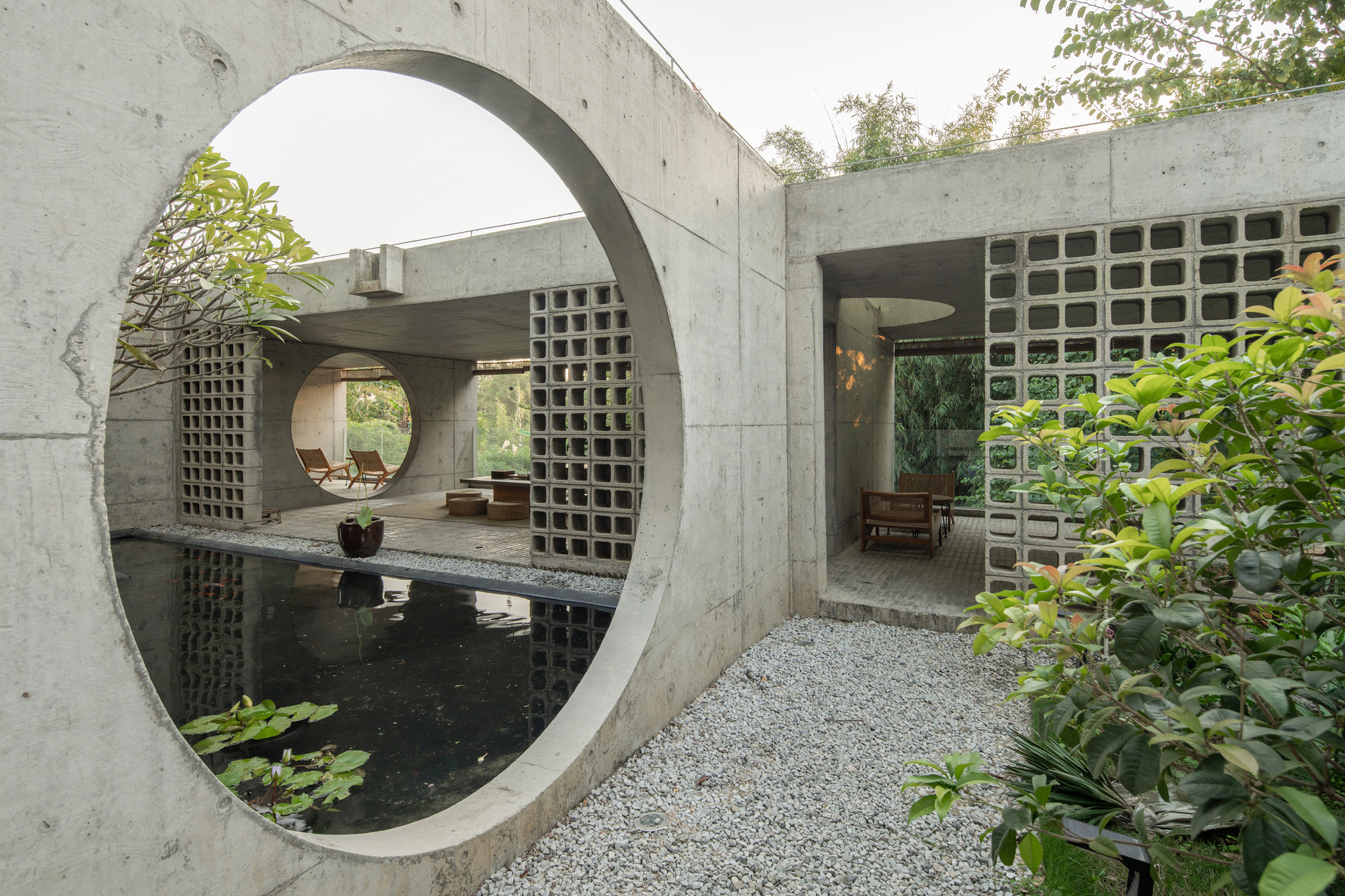 Concrete courtyard with circular openings framing a reflecting pool and perforated brick walls beyond planted beds