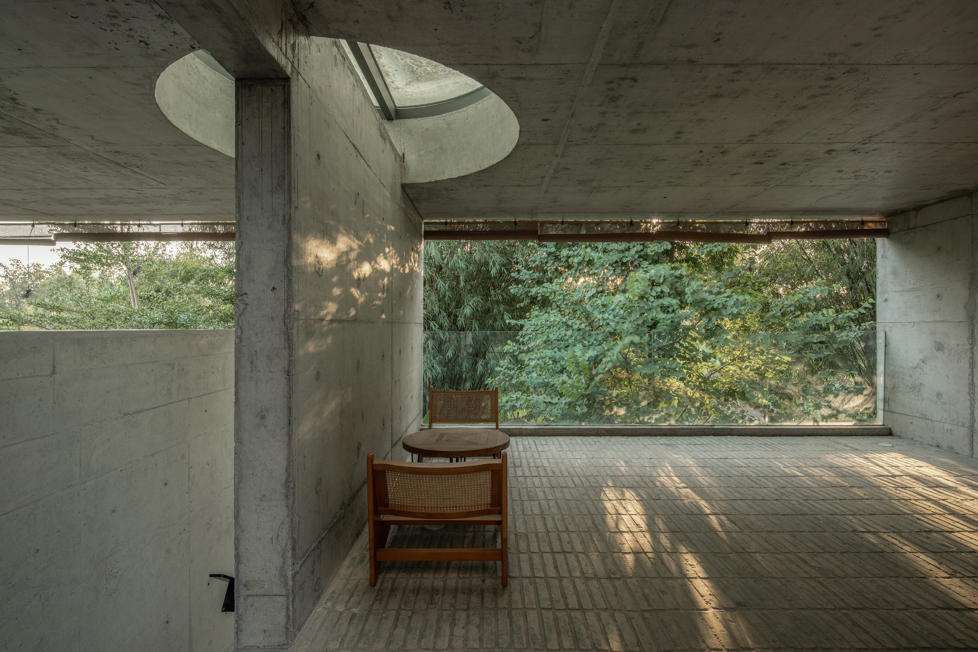 Interior room with curved concrete skylight and brick floor filtering dappled afternoon light