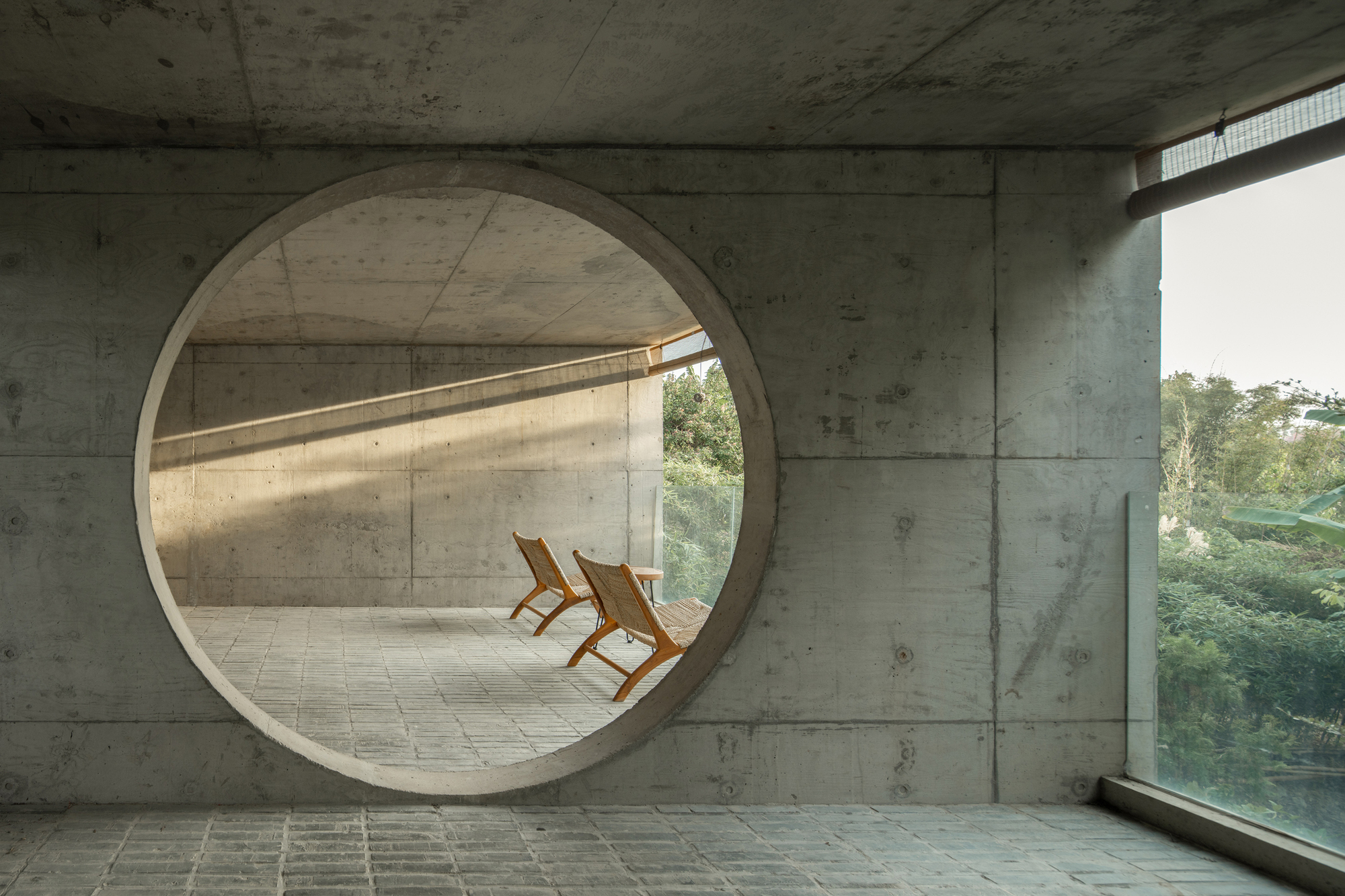 Circular concrete portal framing two wooden chairs on a terrace overlooking dense foliage