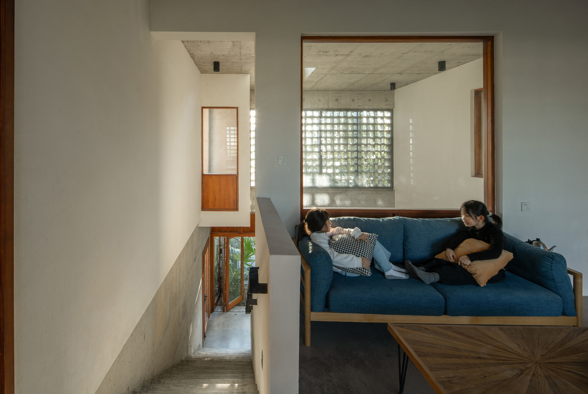 Upper level seating nook with a blue sofa overlooking a stairwell with concrete breeze blocks filtering daylight