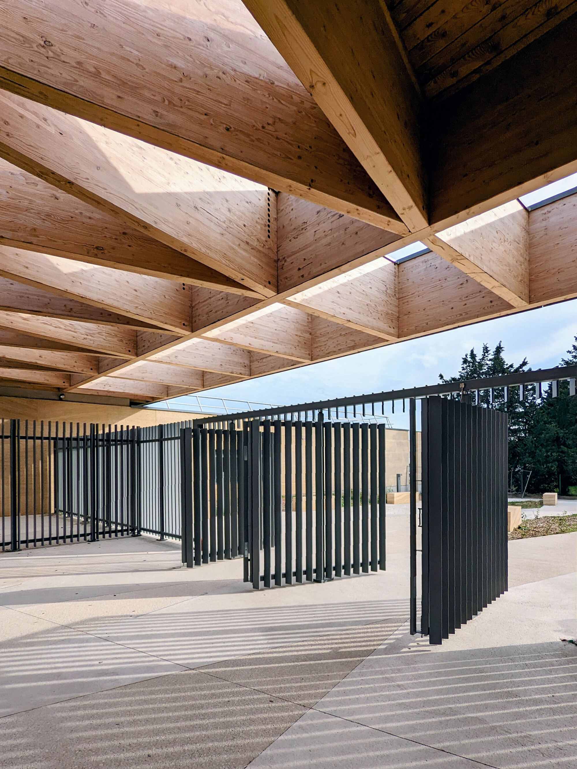 View beneath the timber roof canopy showing vertical black metal screening elements casting shadows