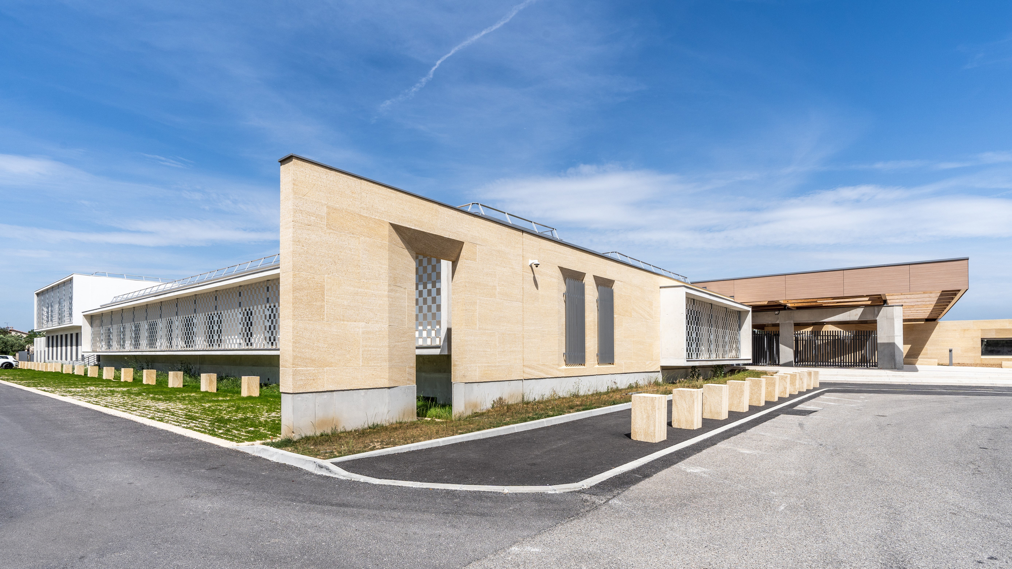 Corner view of the beige masonry facade with patterned screen panels and planted gravel beds