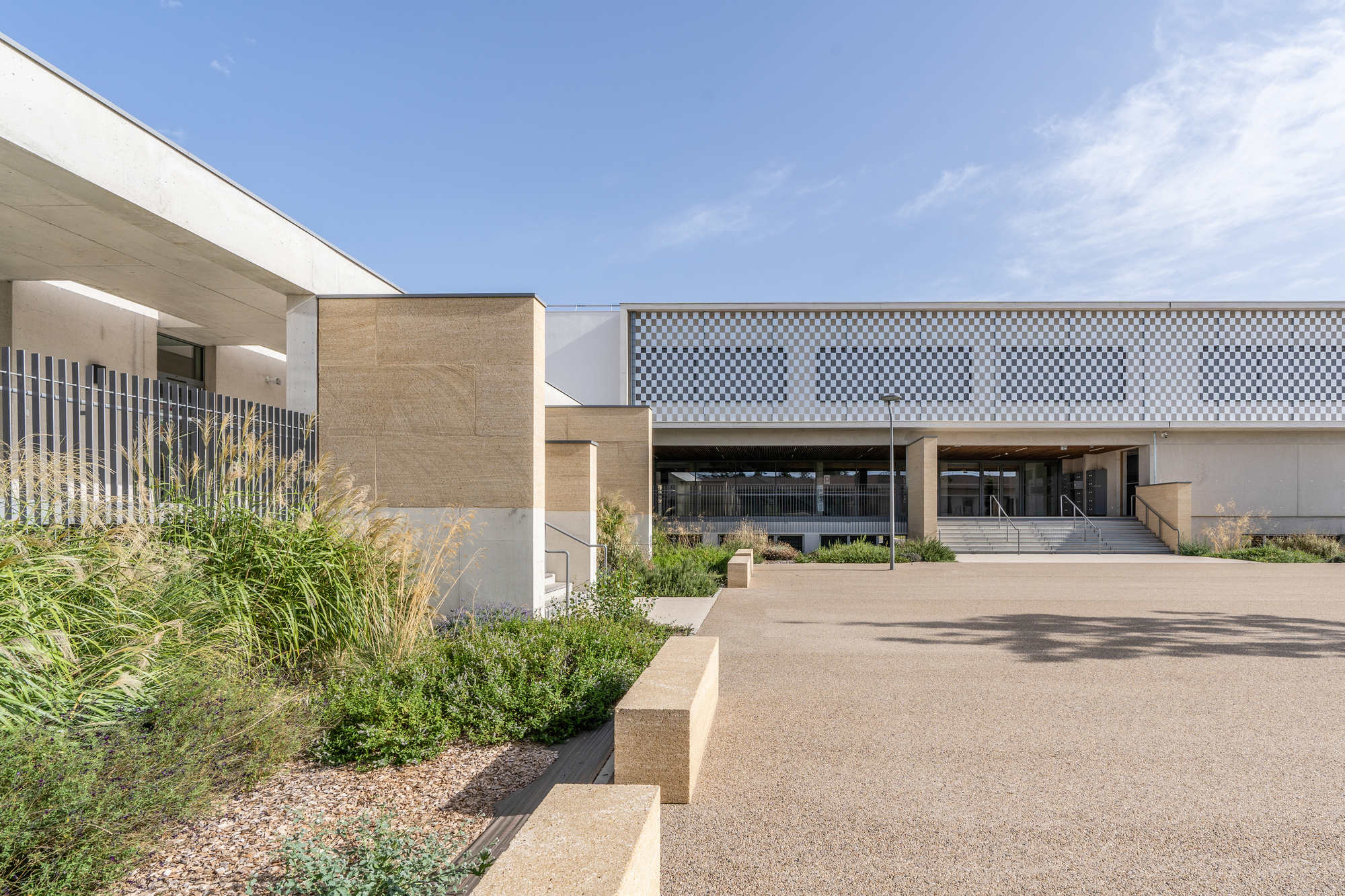 Entry drive framed by gravel beds with grasses and chequered facade screen panel
